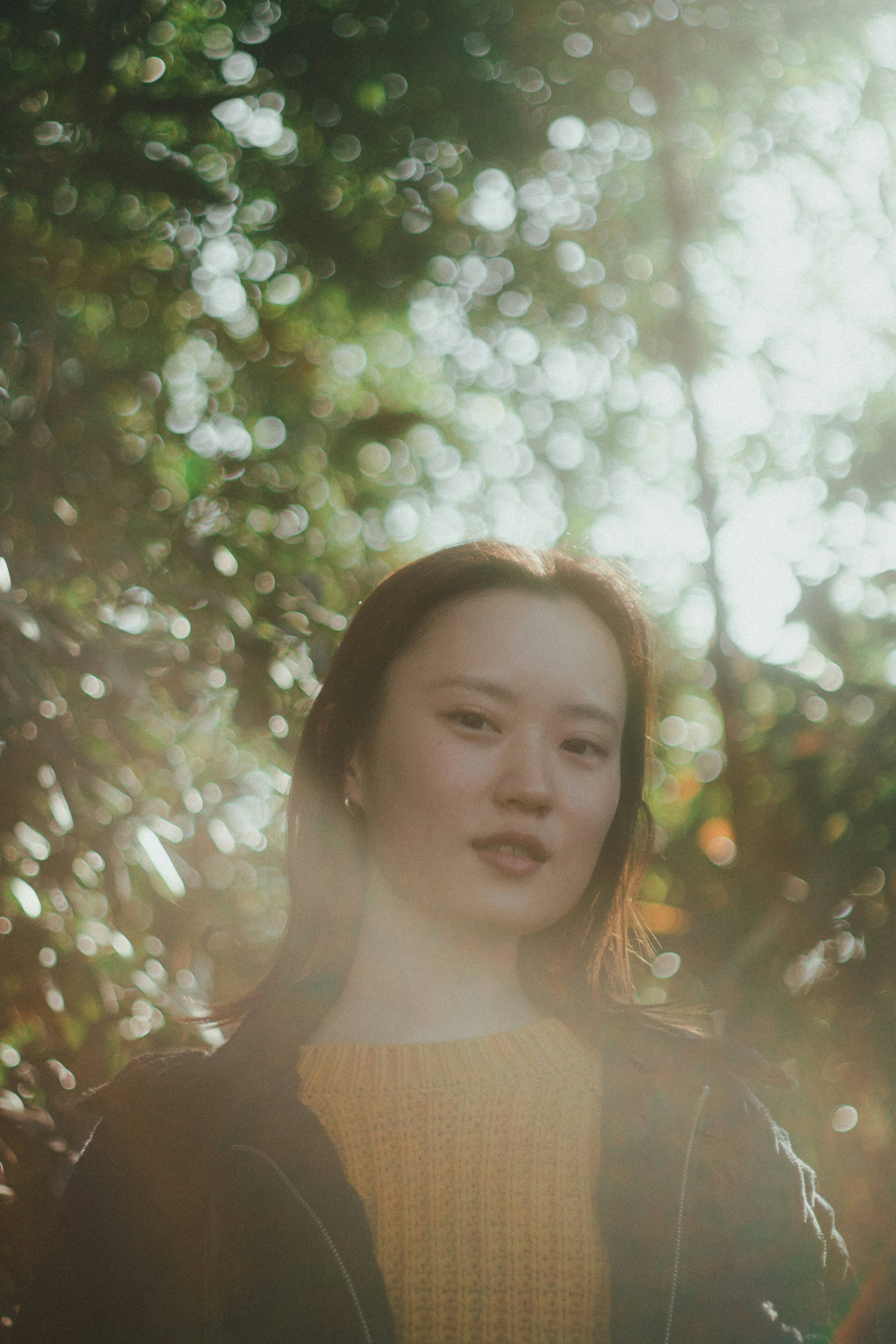 Portrait of a woman smiling in soft natural light She wears a yellow sweater with blurred green leaves in the background