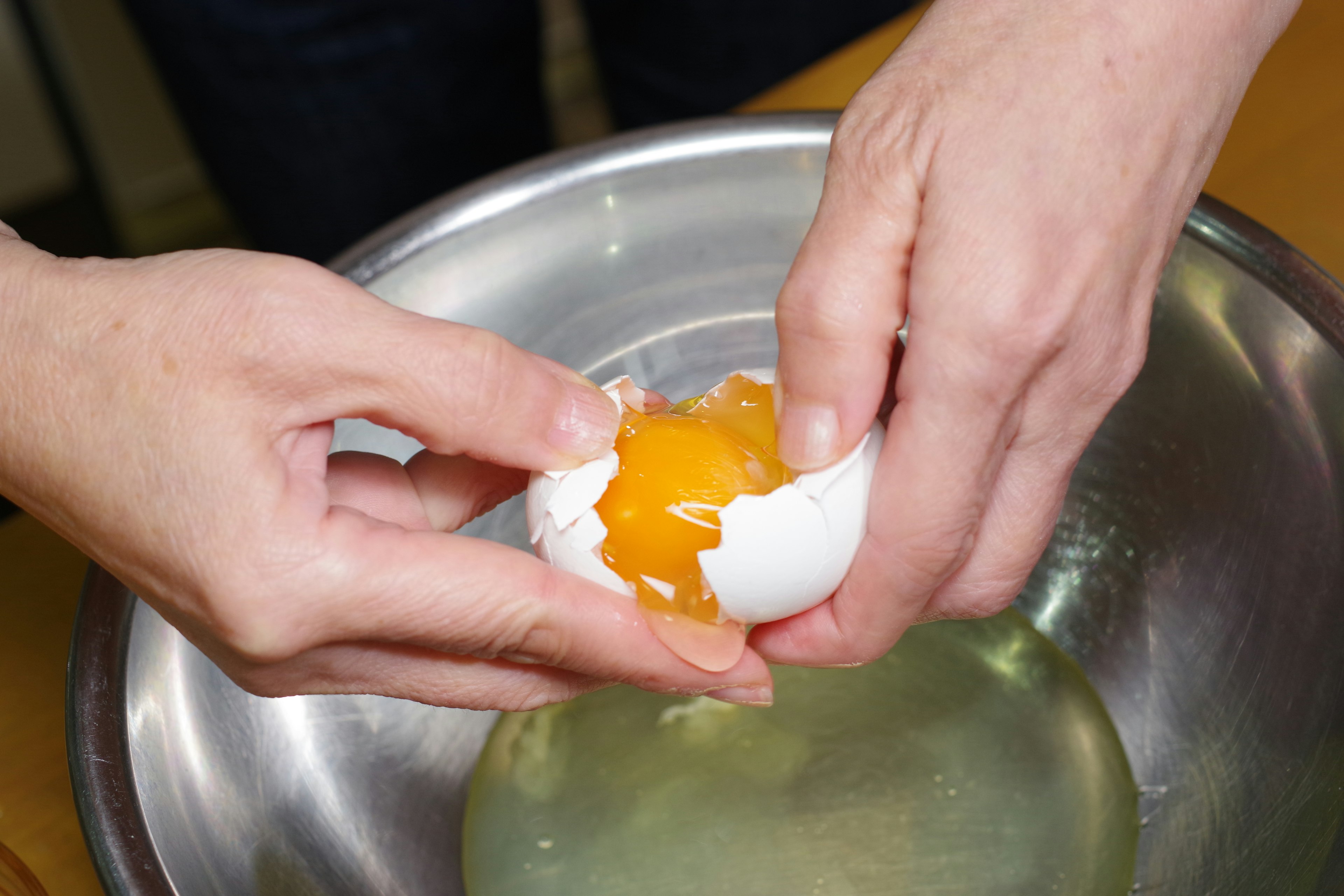 Hands cracking an egg with visible yolk in a bowl