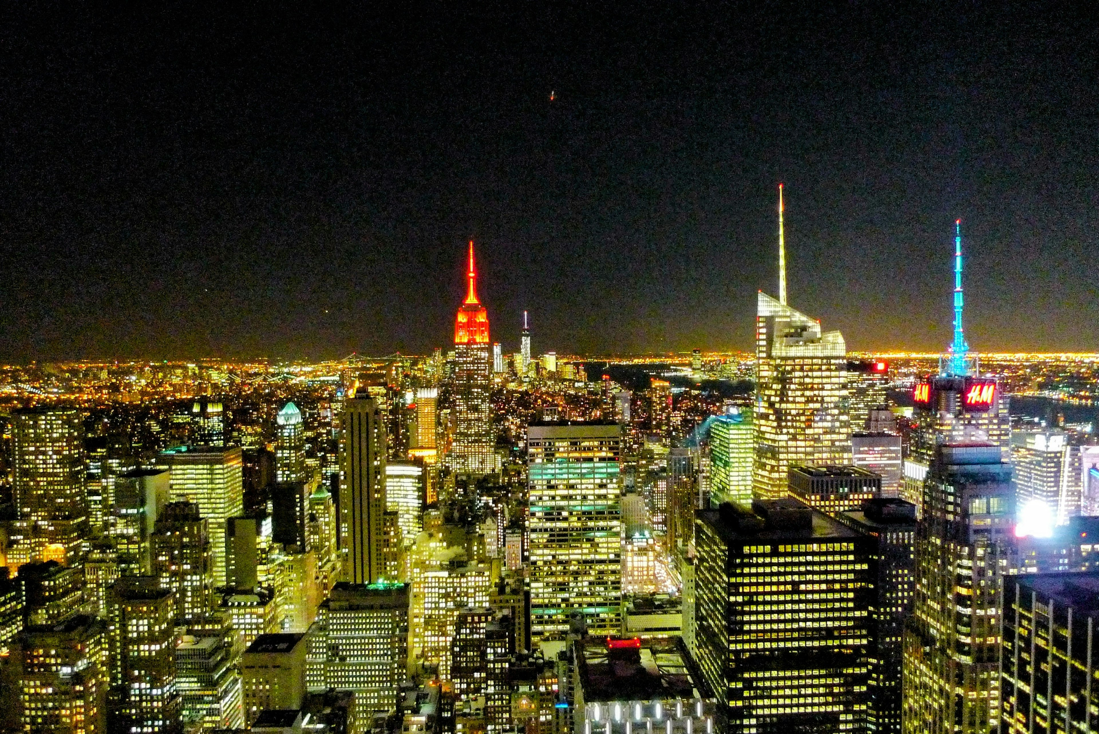 Beeindruckende nächtliche Skyline von New York mit dem rot beleuchteten Empire State Building und blau beleuchteten Türmen