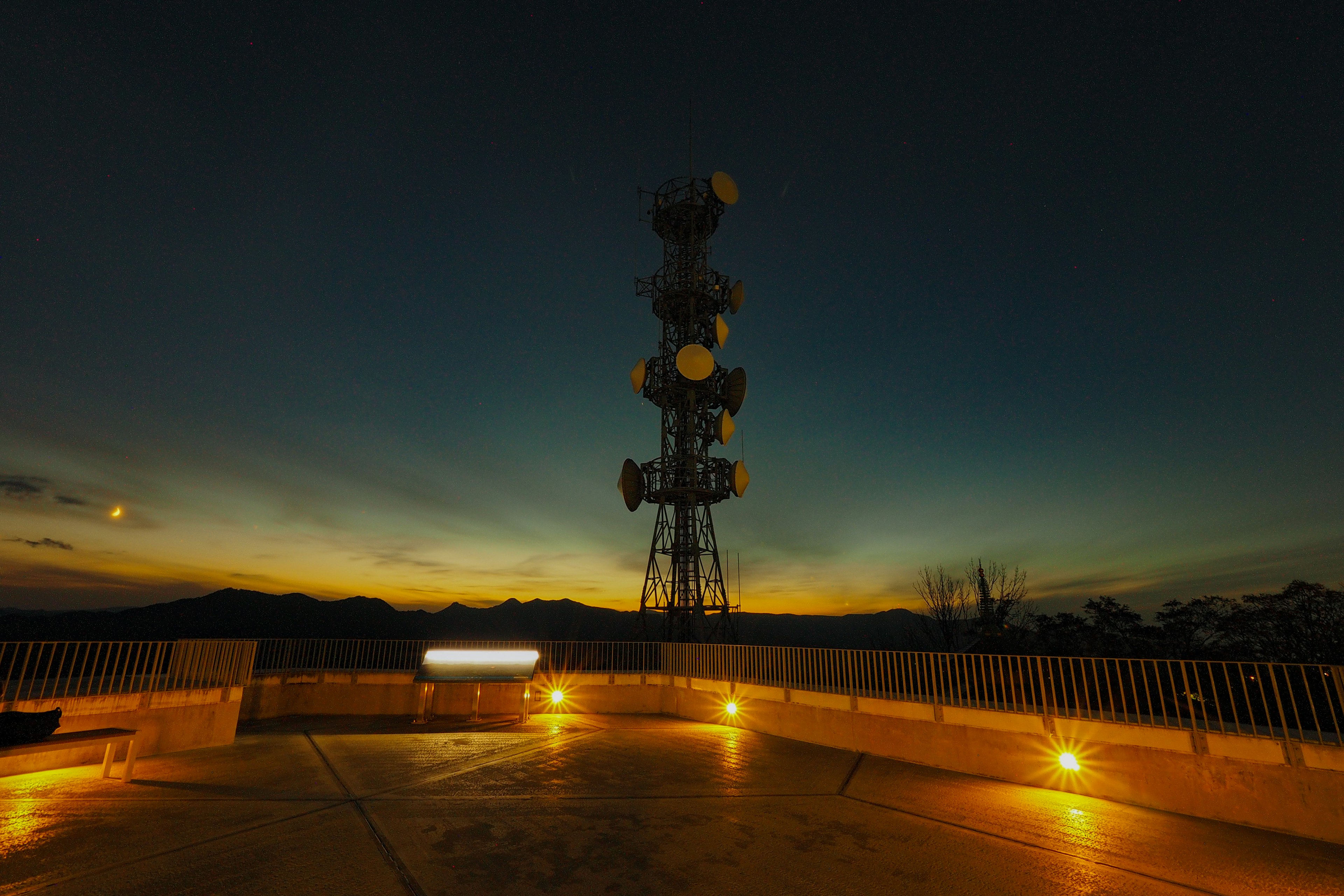 Torre de comunicaciones en silueta contra un cielo crepuscular con luces circundantes