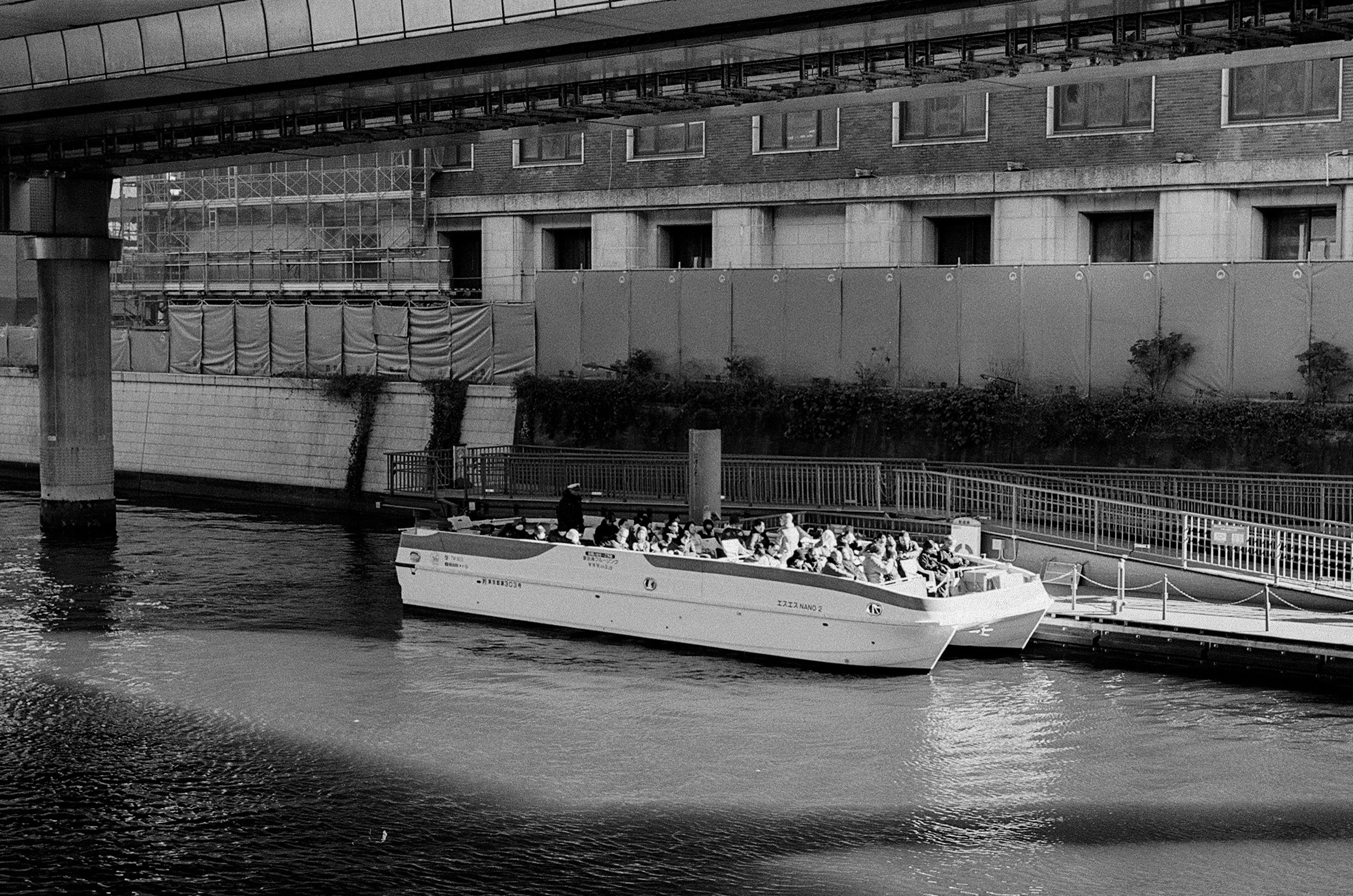 Imagen en blanco y negro de un barco atracado en un río con edificios circundantes