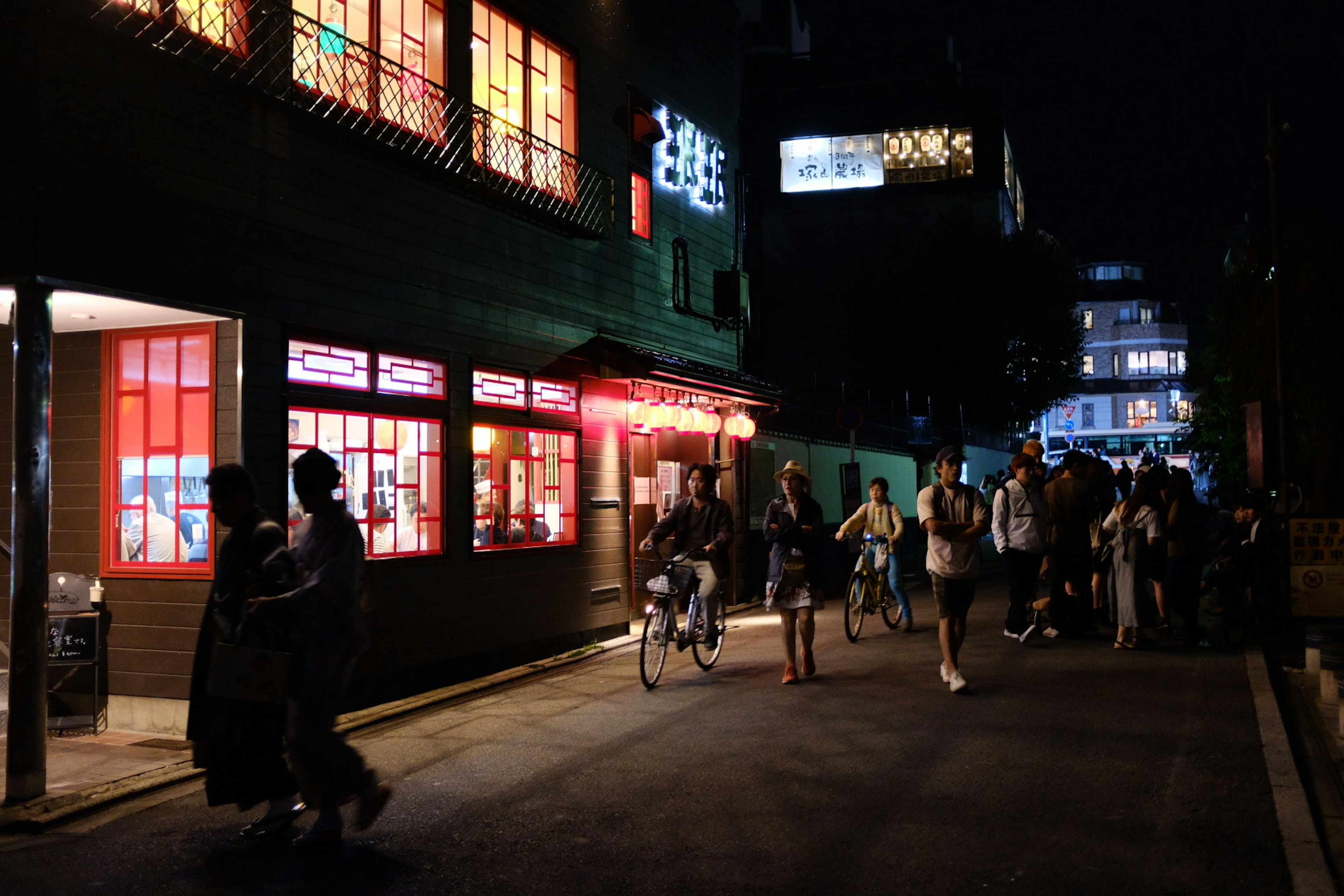 Scena di strada vivace di notte con un ristorante dalle finestre rosse e pedoni