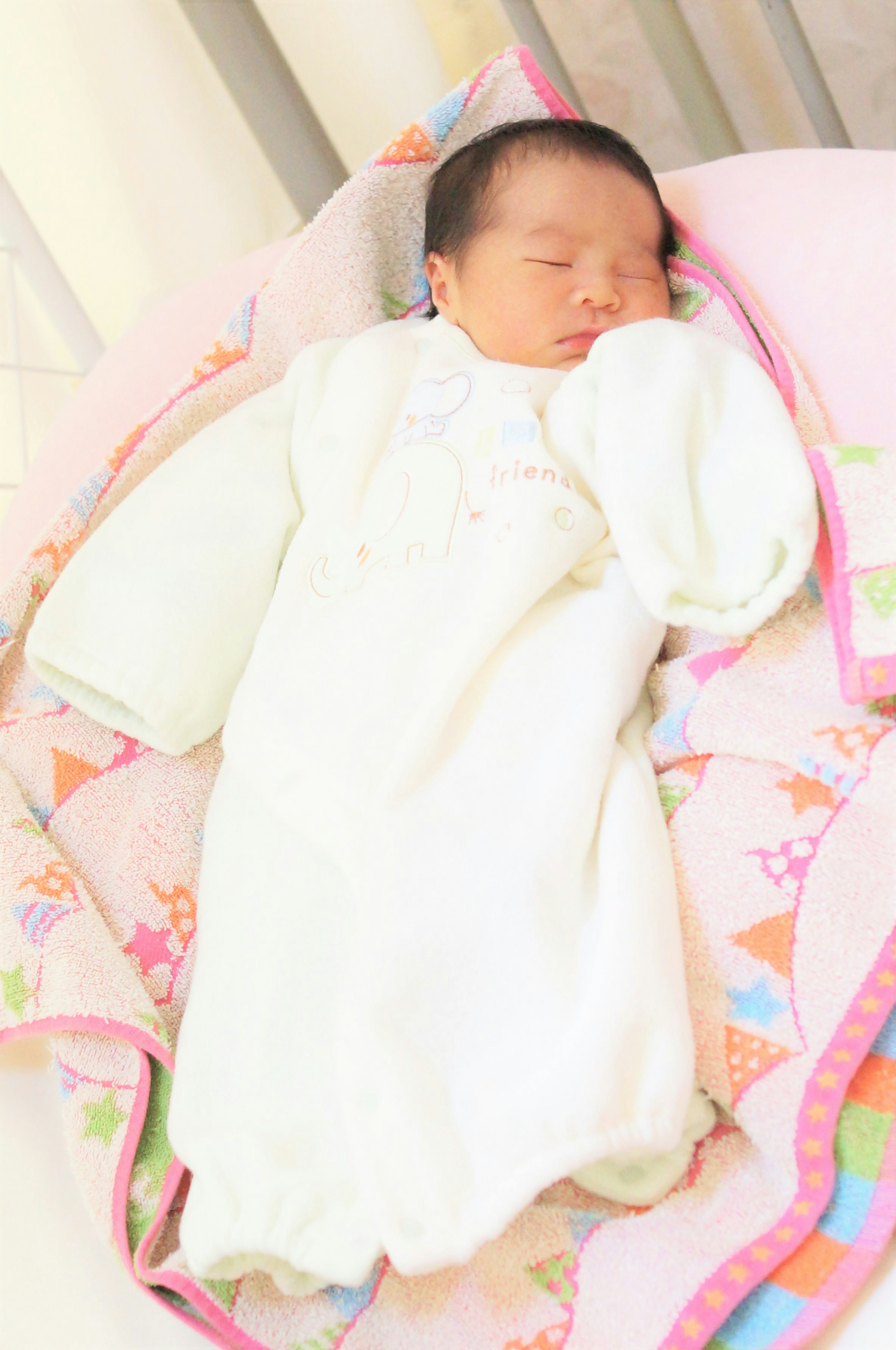 A sleeping baby in a white outfit on a colorful blanket