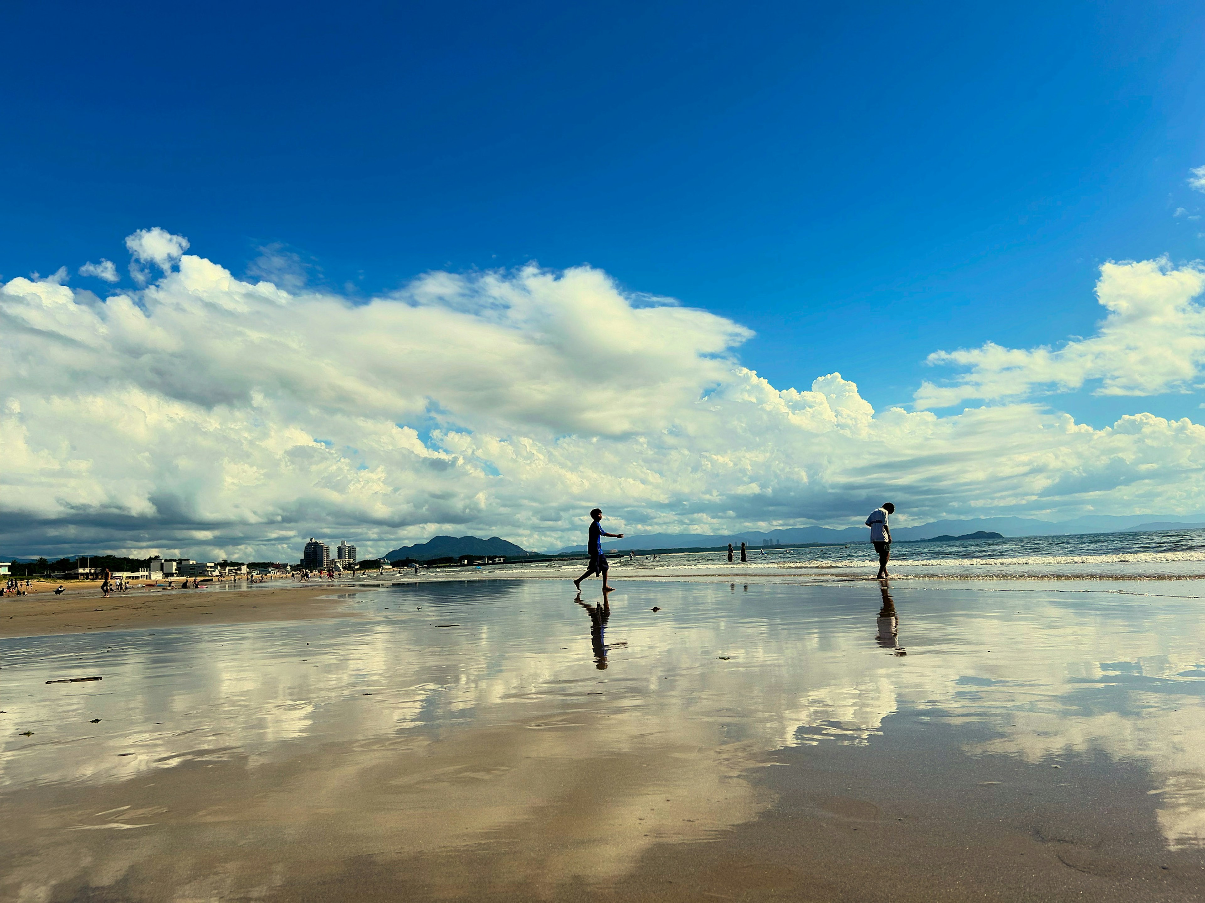 Two people walking on a beach reflecting the blue sky and clouds