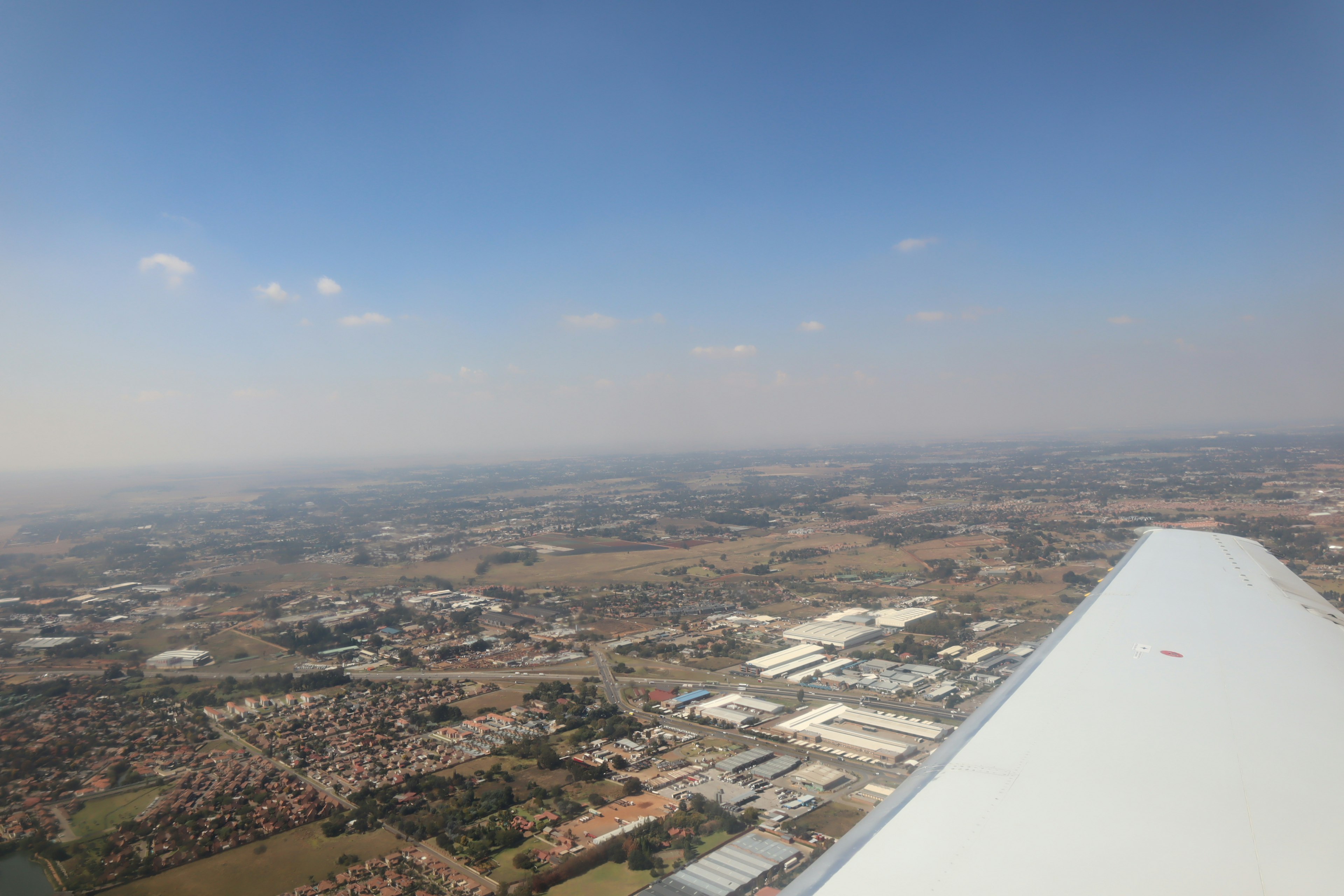 Luftaufnahme von einem Flugzeugflügel mit weiten Landschaften und blauem Himmel