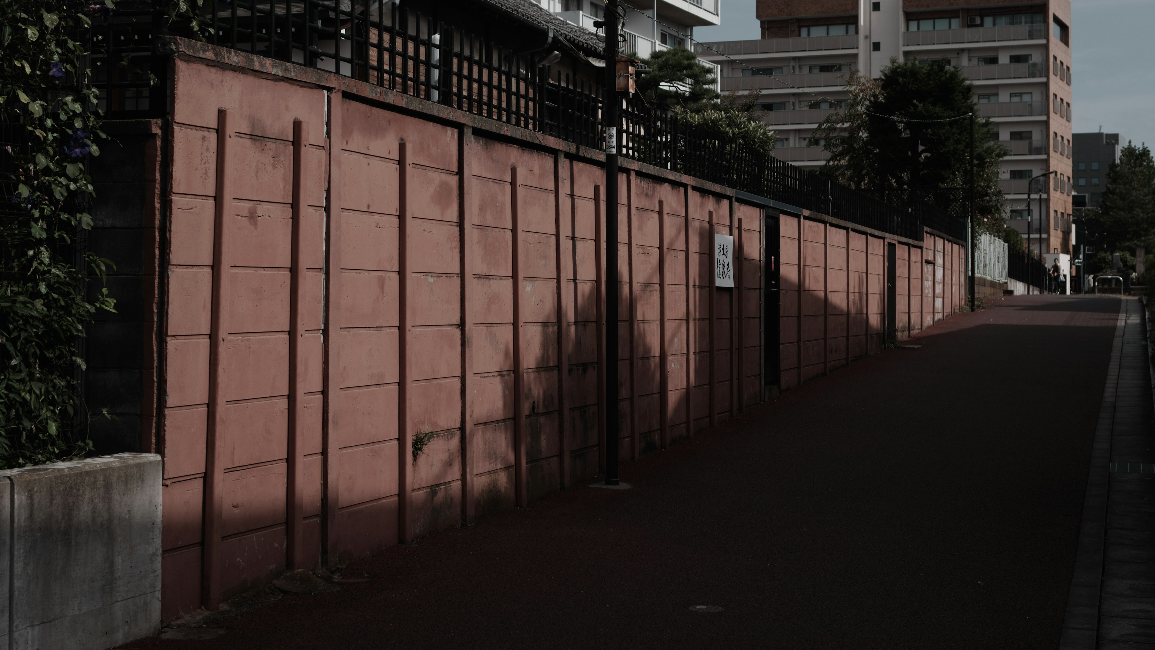 Narrow path with a light red wall and shadows created by nearby buildings