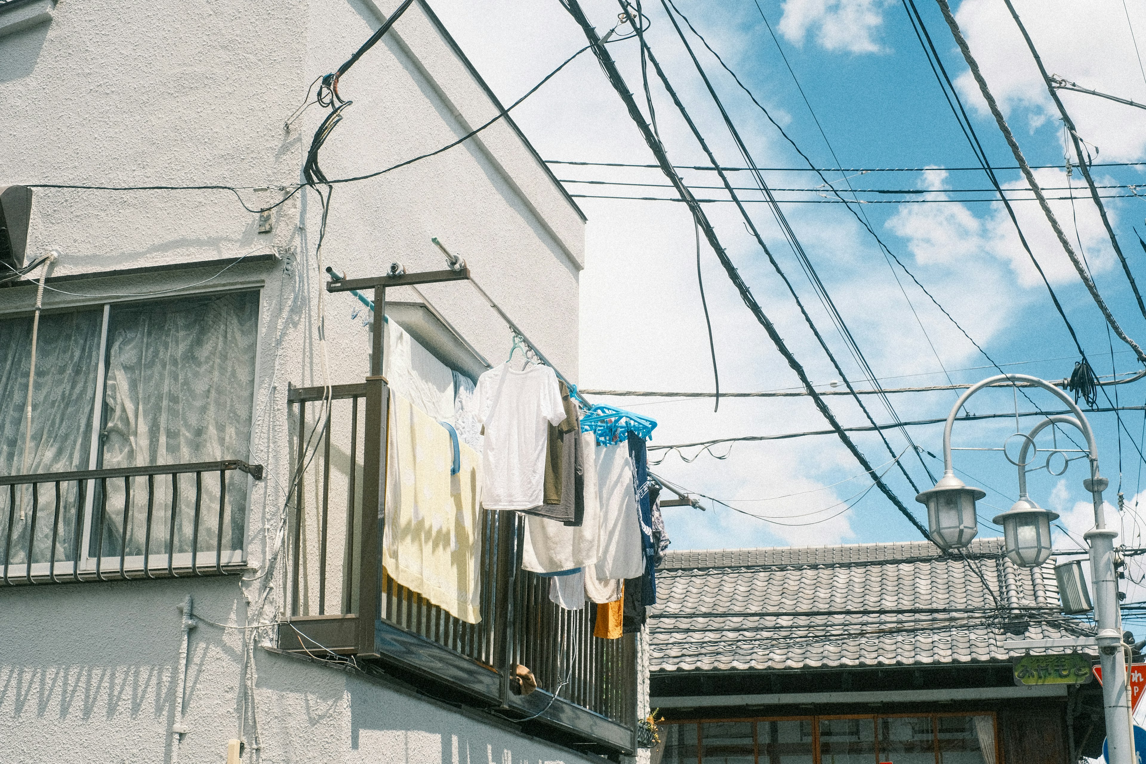 Casa de pared blanca con ropa colgada en el balcón cielo azul y líneas eléctricas visibles