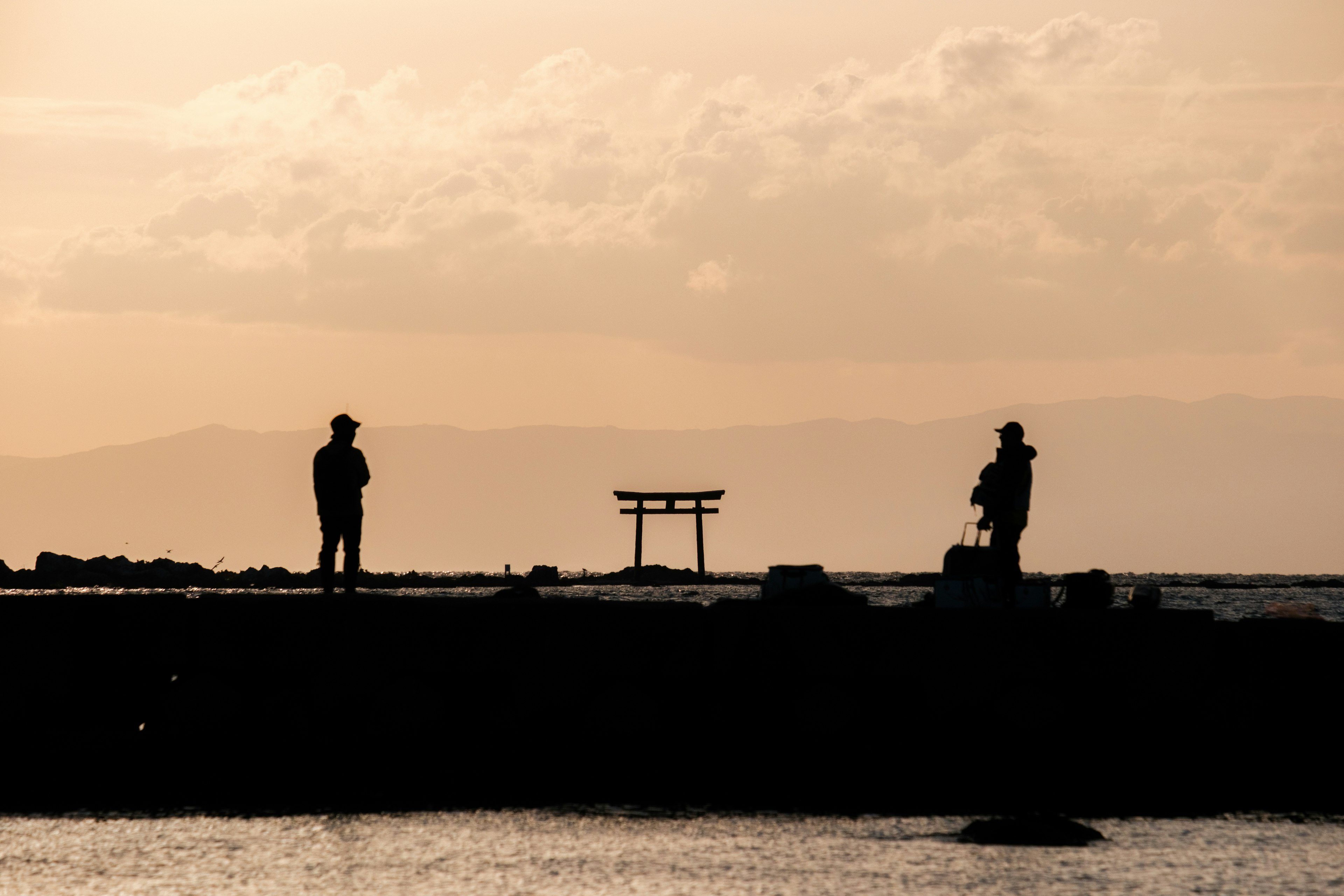 Silhouettes de deux personnes au coucher de soleil avec un torii