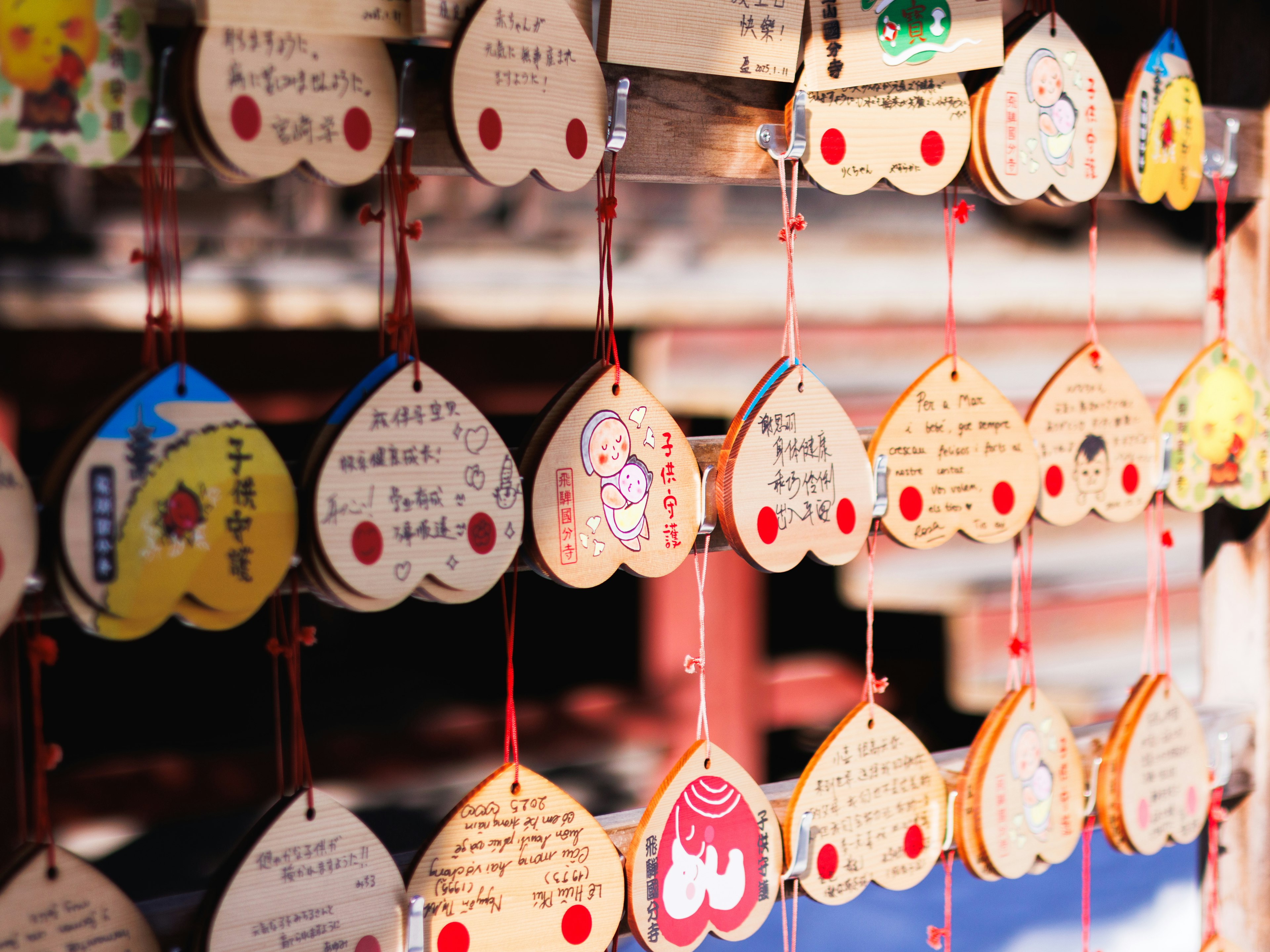 Colorful ema plaques hanging in a shrine with various designs and messages