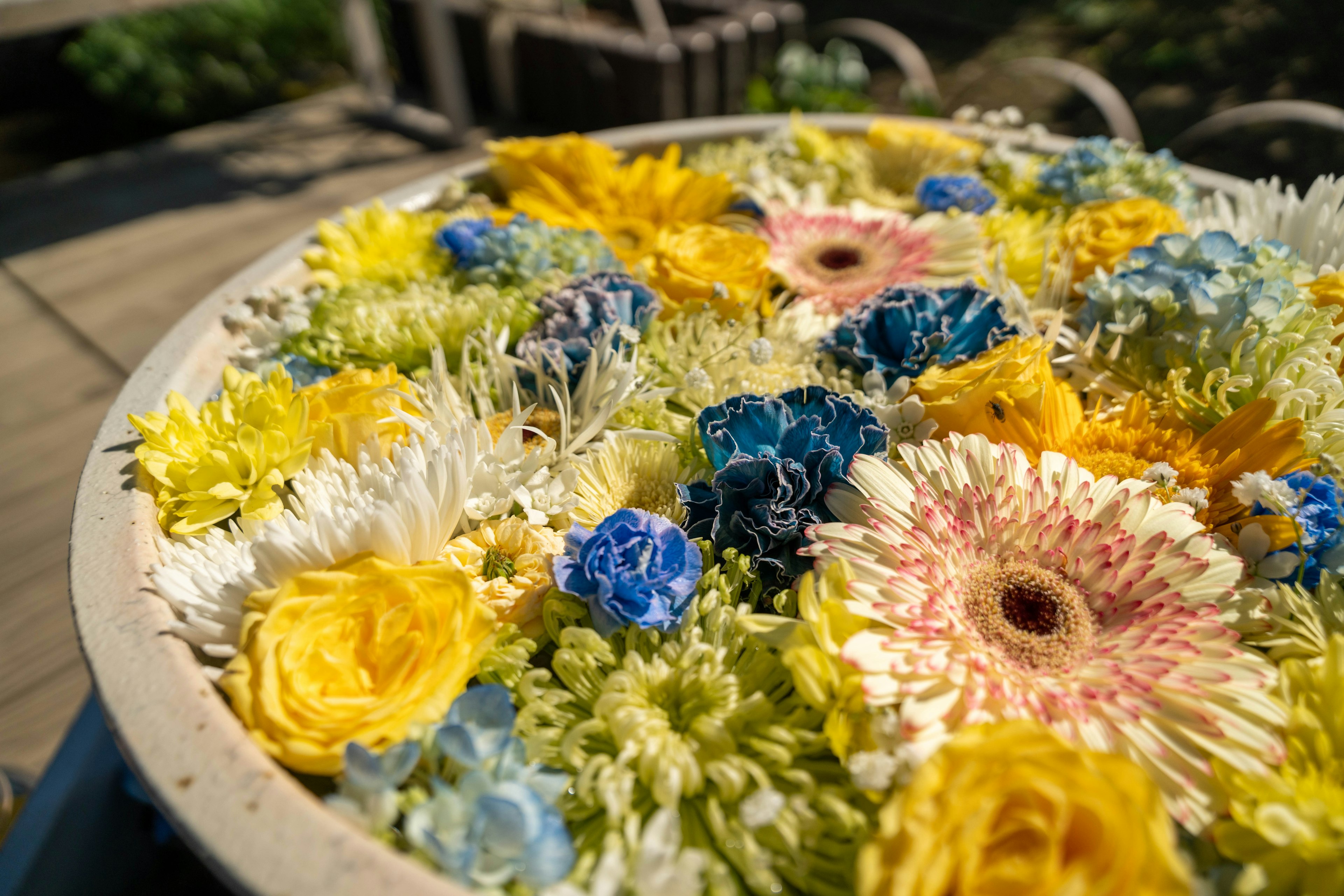 A vibrant arrangement of flowers featuring yellow and blue blooms in a decorative bowl