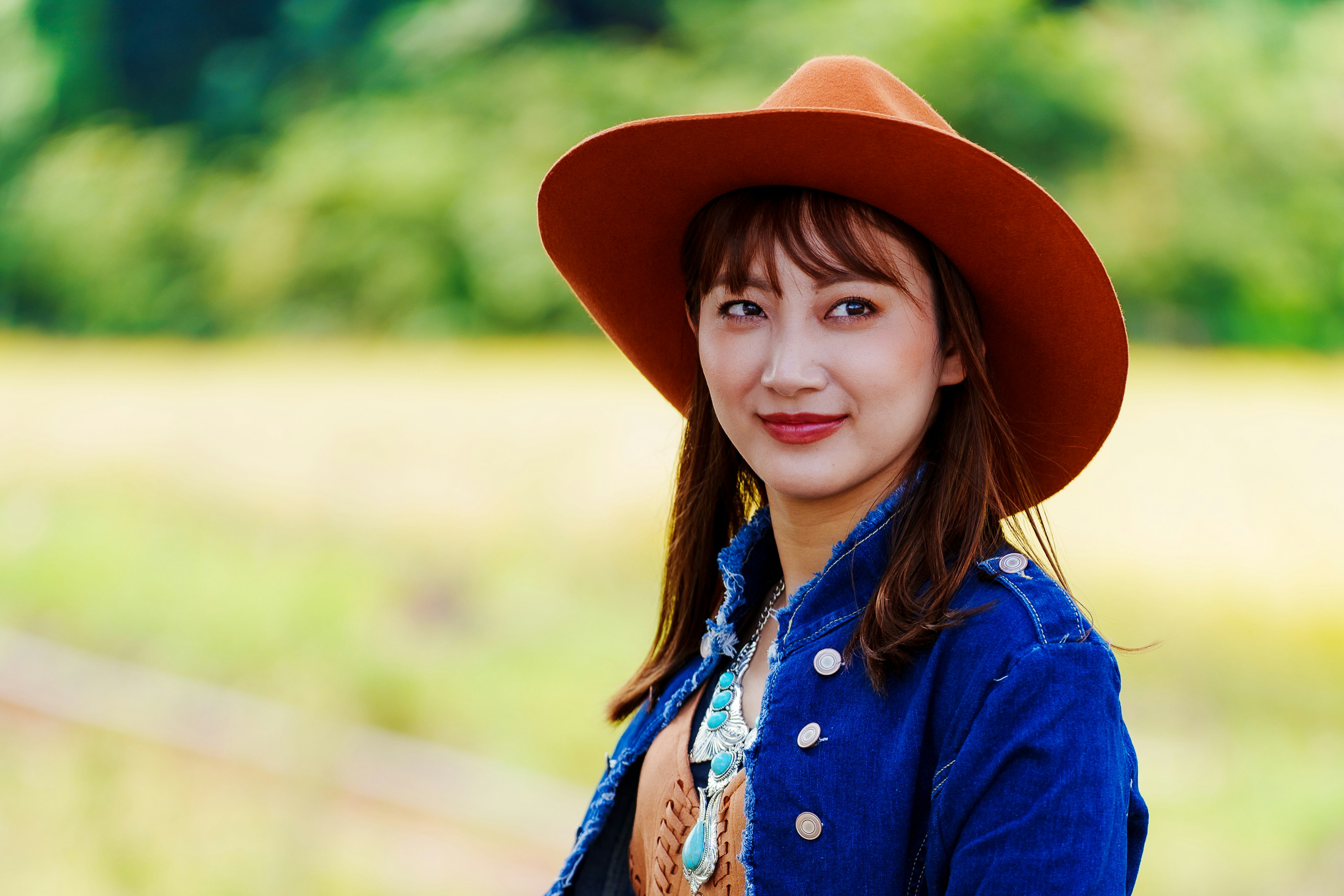 Donna con giacca di jeans e cappello arancione che sorride in uno sfondo pittoresco