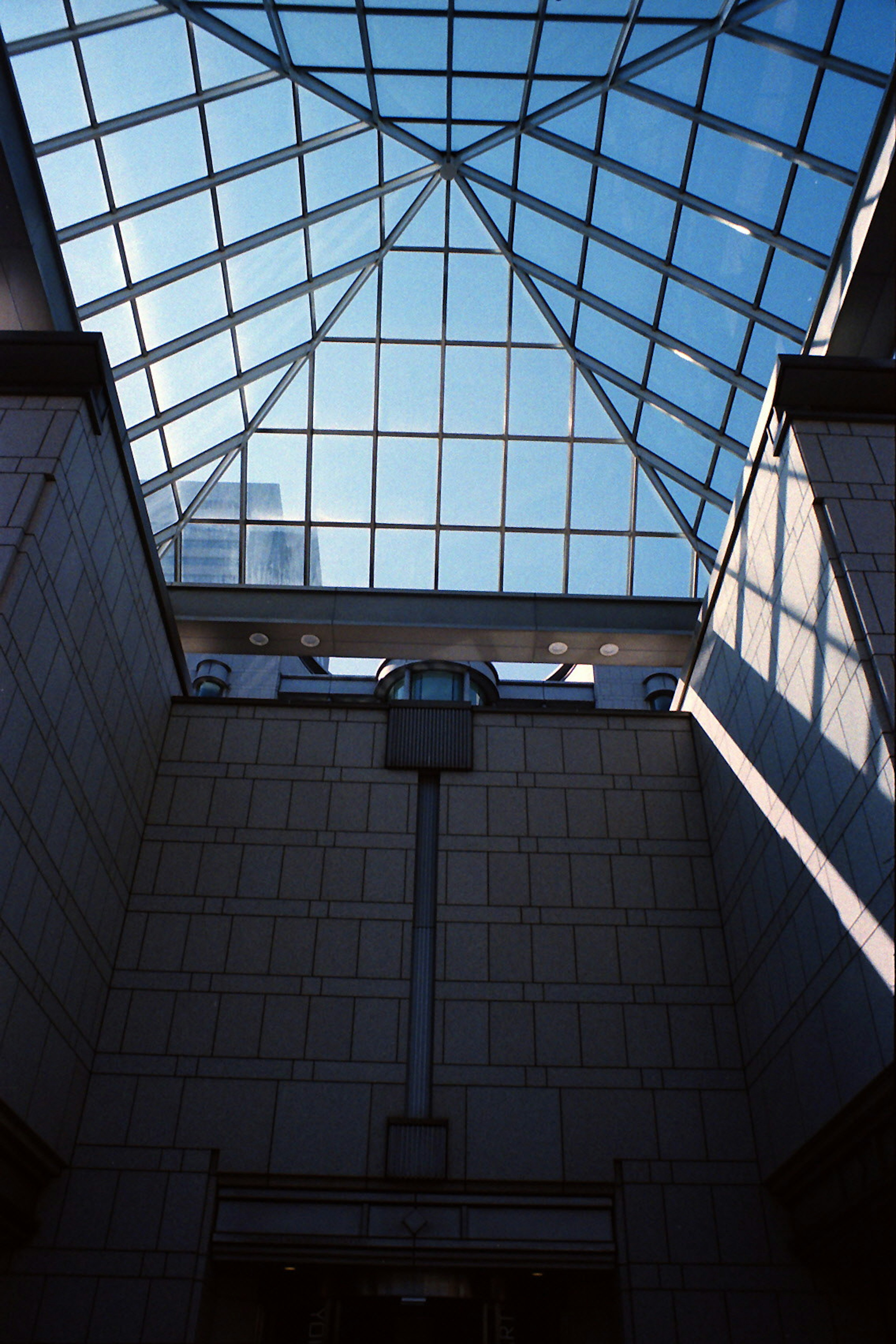 View looking up from below a glass roof with geometric patterns and building shadows