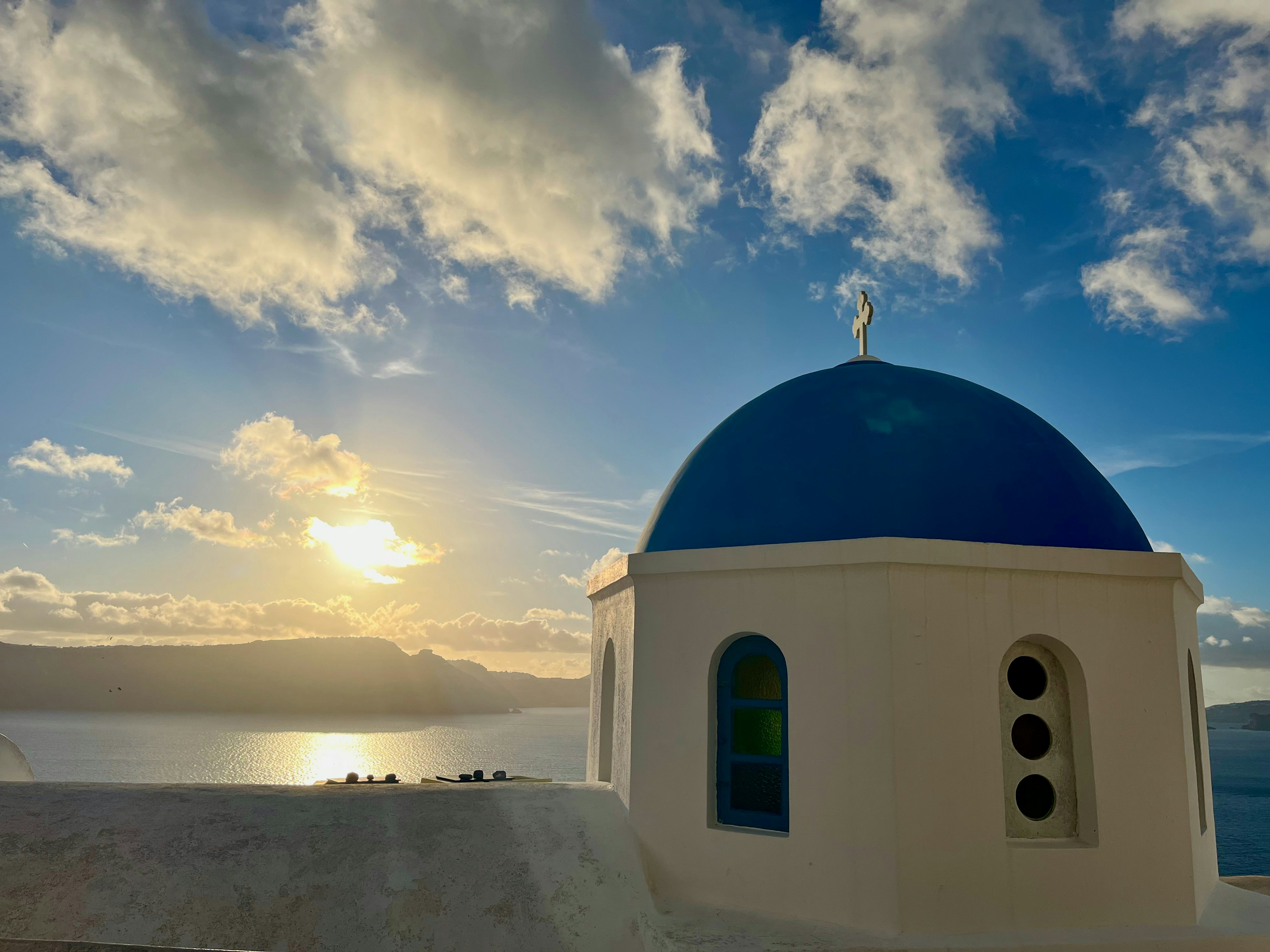 Bangunan putih dengan kubah biru yang diterangi oleh matahari terbenam di Santorini