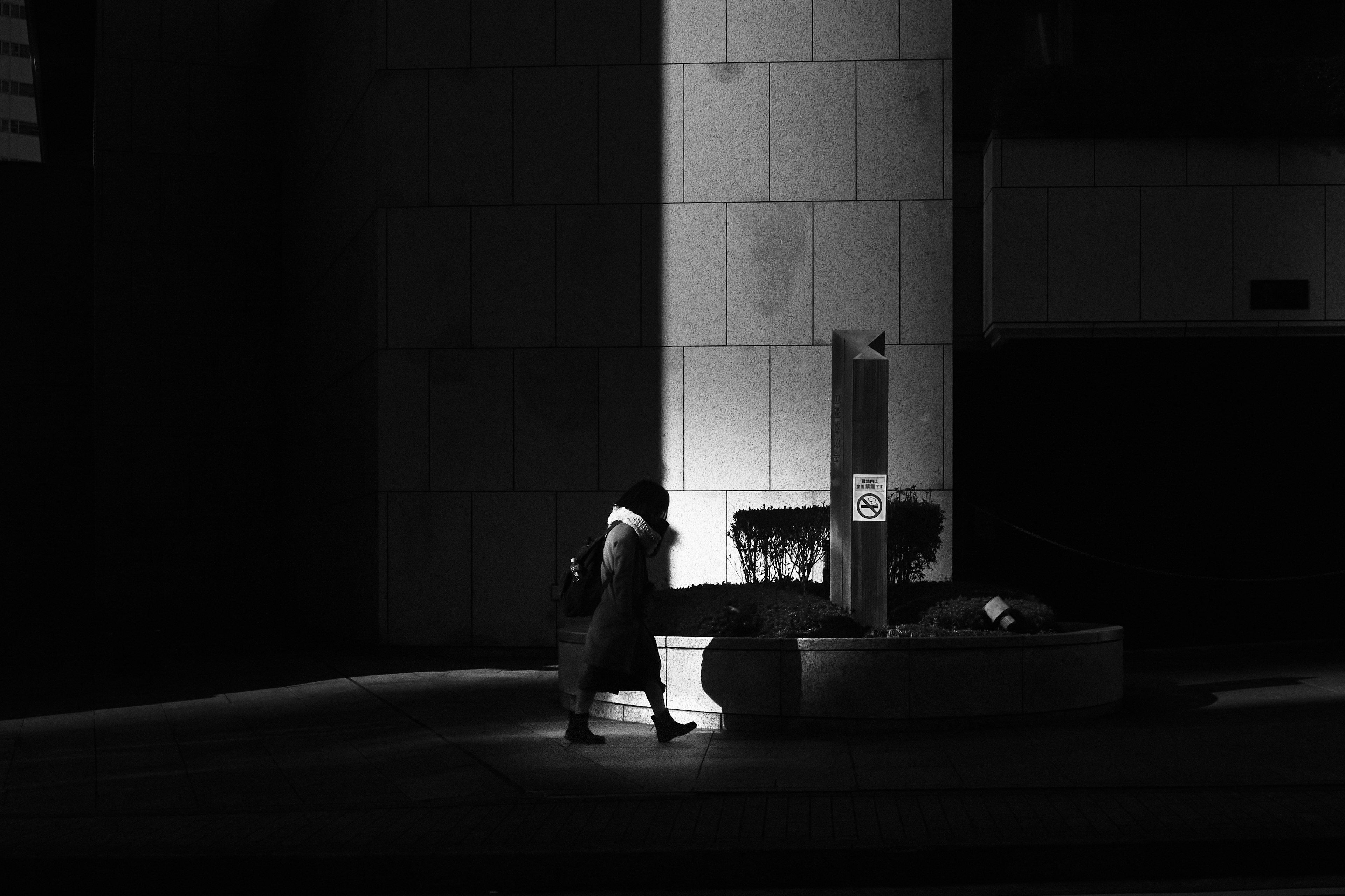 Silhouette of a person walking in a dark urban setting with a bright column