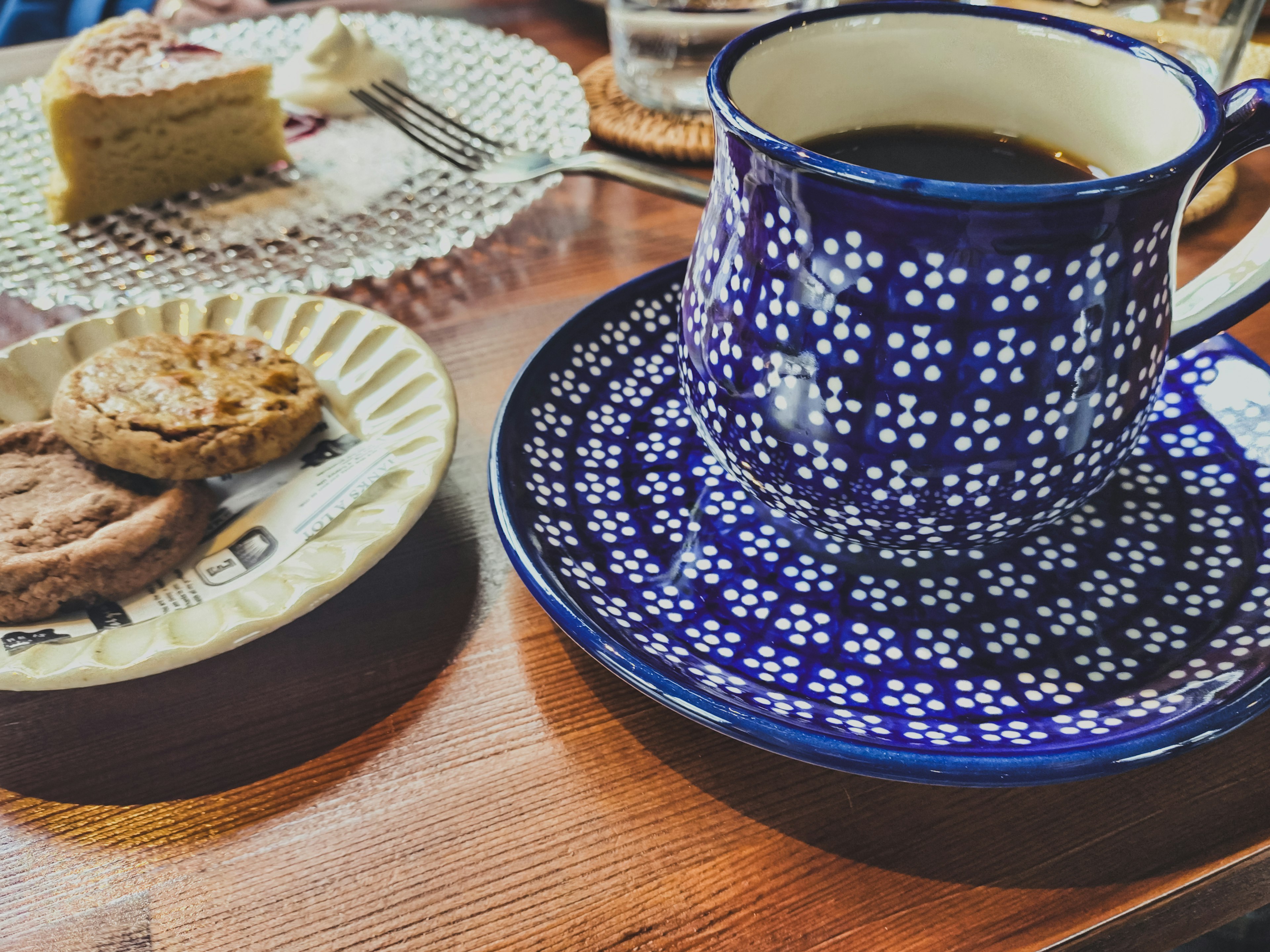 Kopi dalam cangkir bermotif biru dengan kue di piring