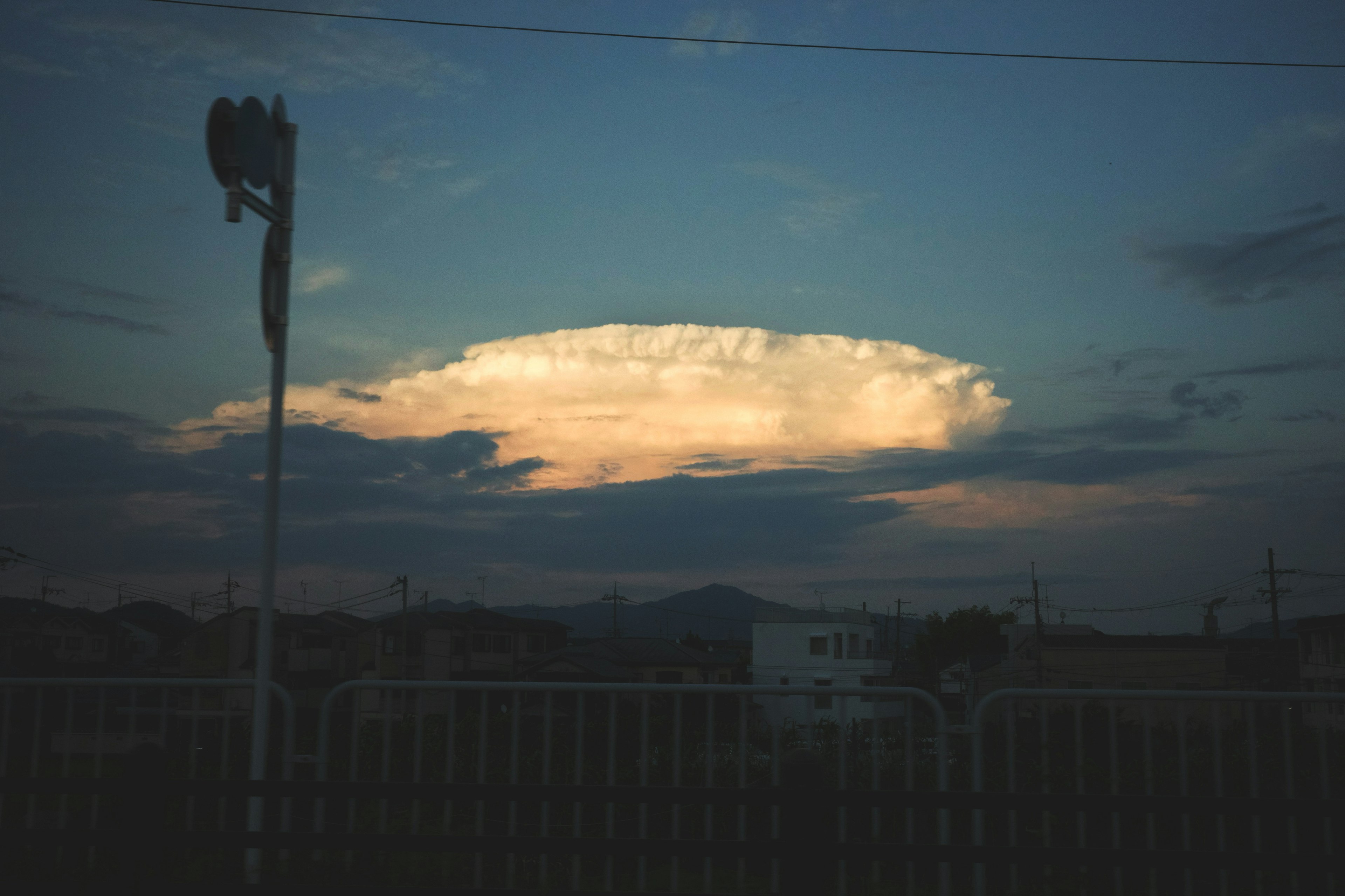 Große Wolke, die vom Sonnenuntergang beleuchtet wird, mit Silhouetten von Gebäuden im Vordergrund