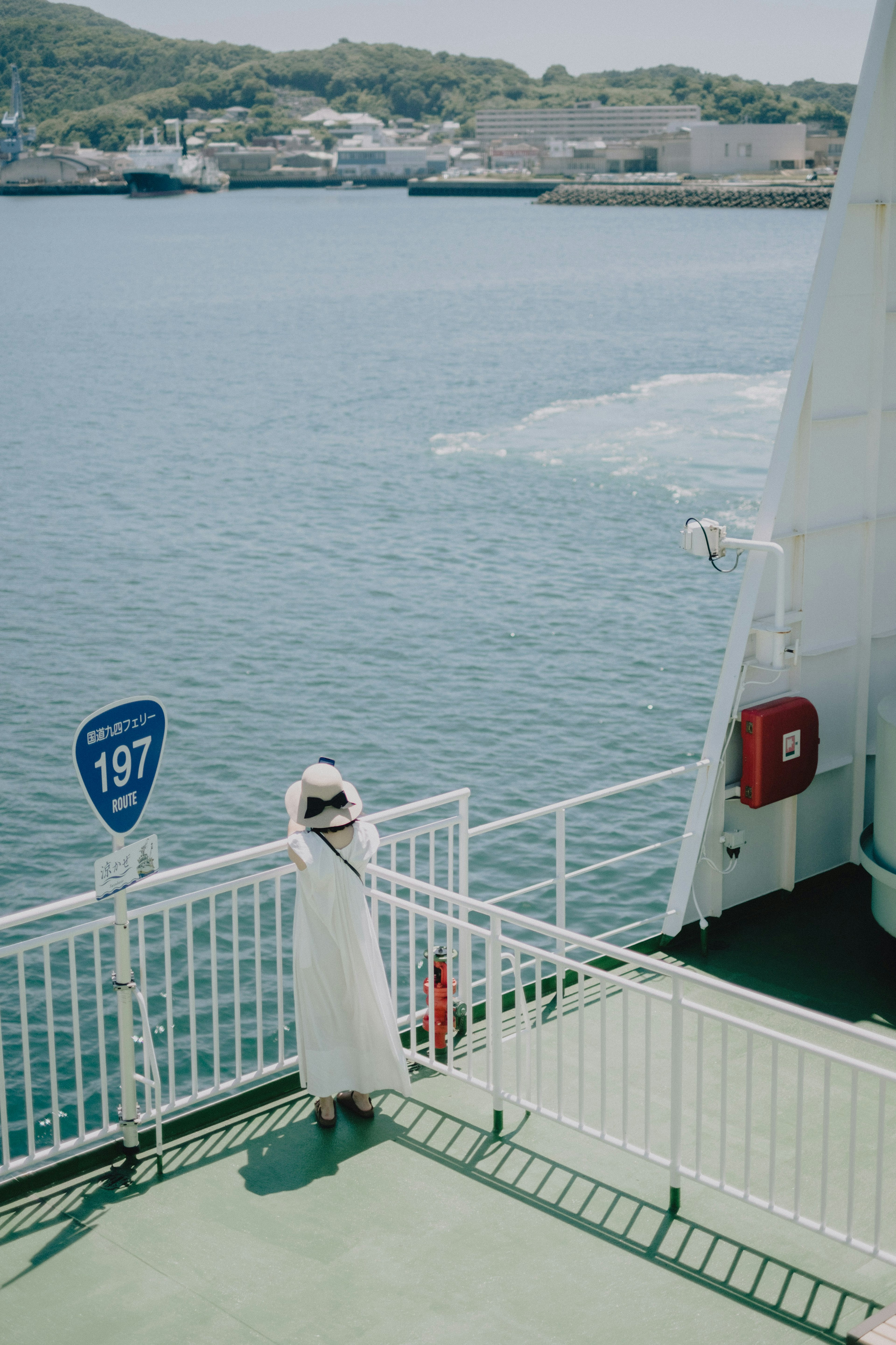 A woman in a white dress looking at the sea from the ferry deck