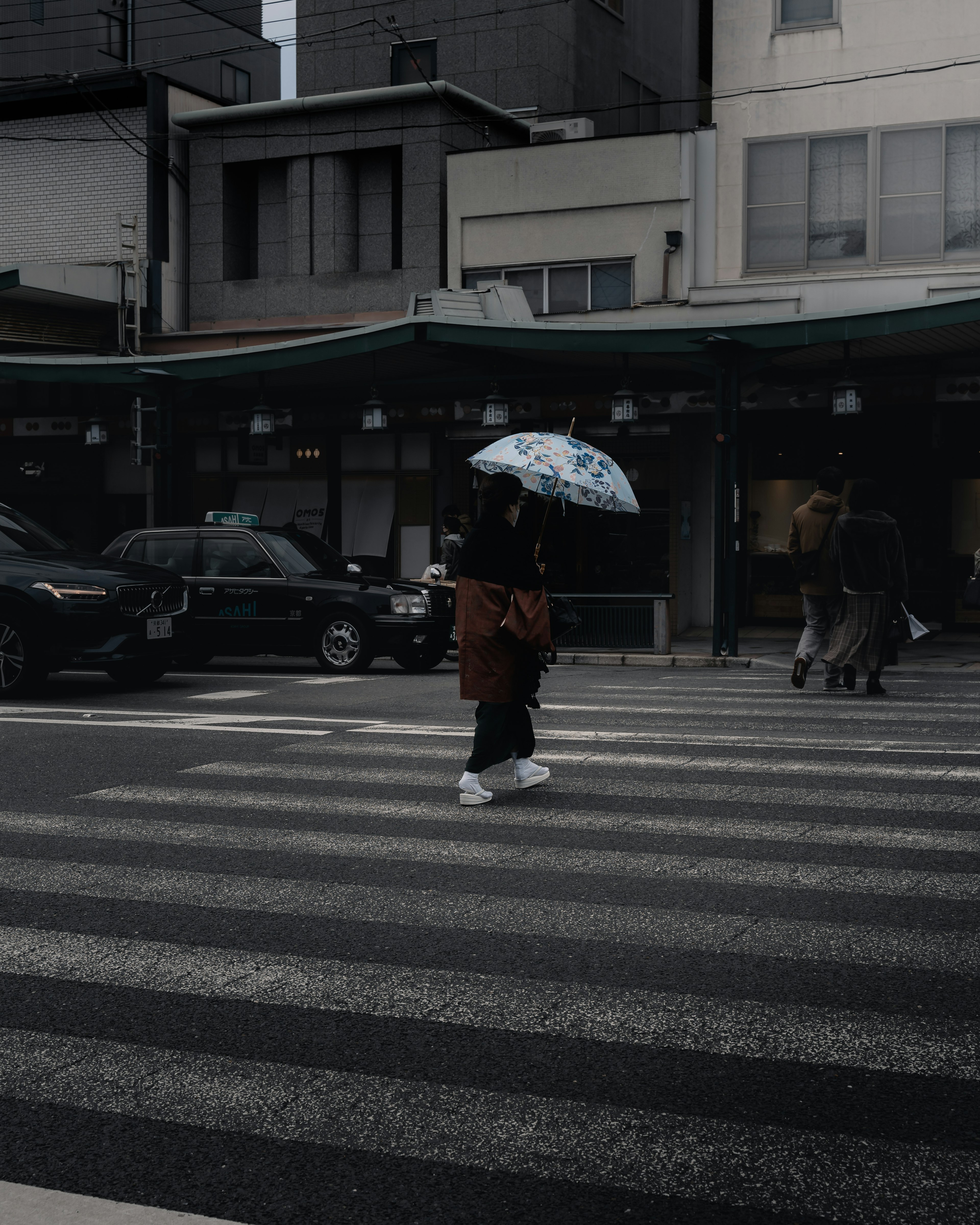 A person walking with an umbrella across a crosswalk