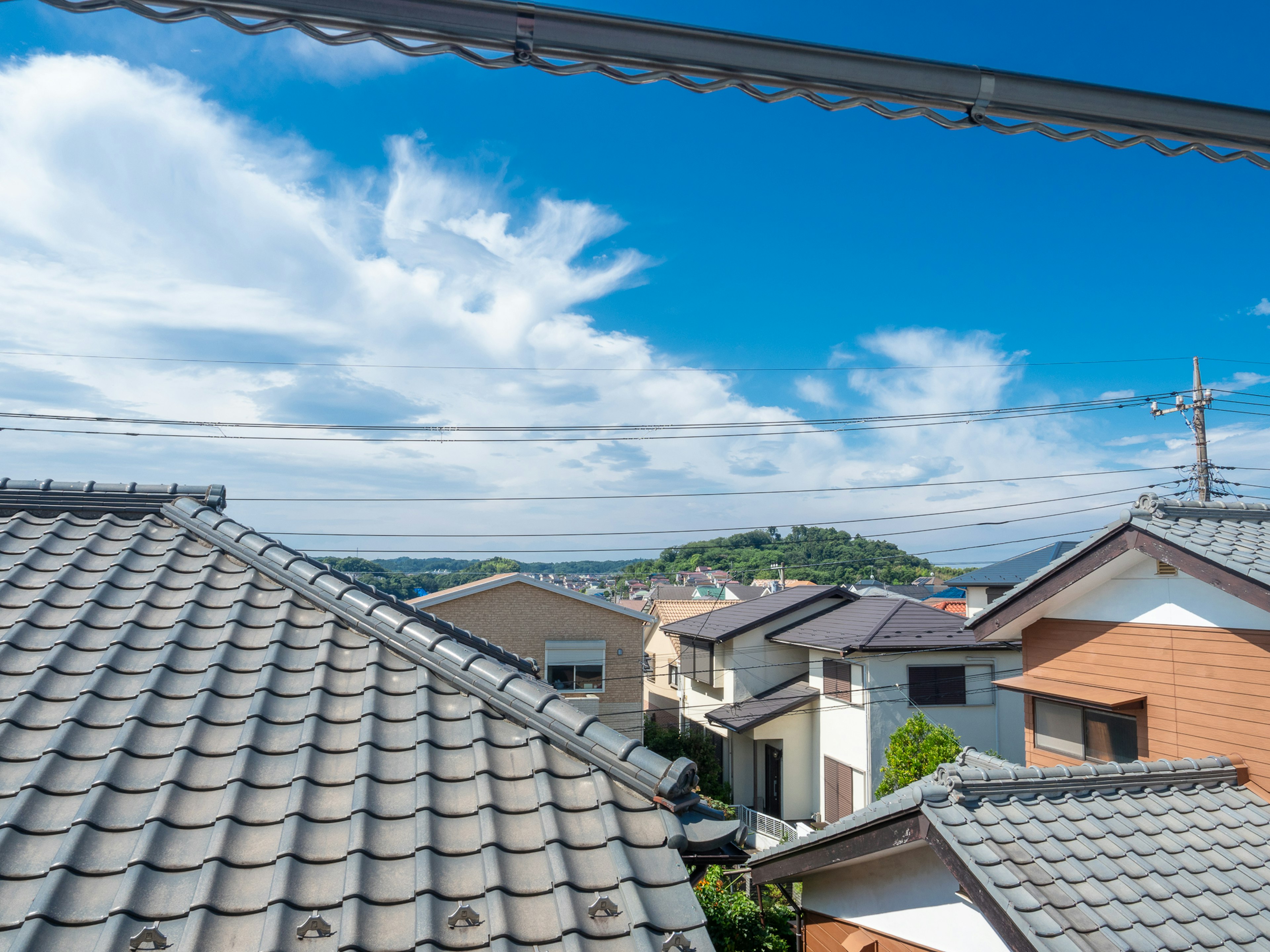 Blick auf ein japanisches Wohngebiet unter einem blauen Himmel mit Ziegeldächern und einem Hügel