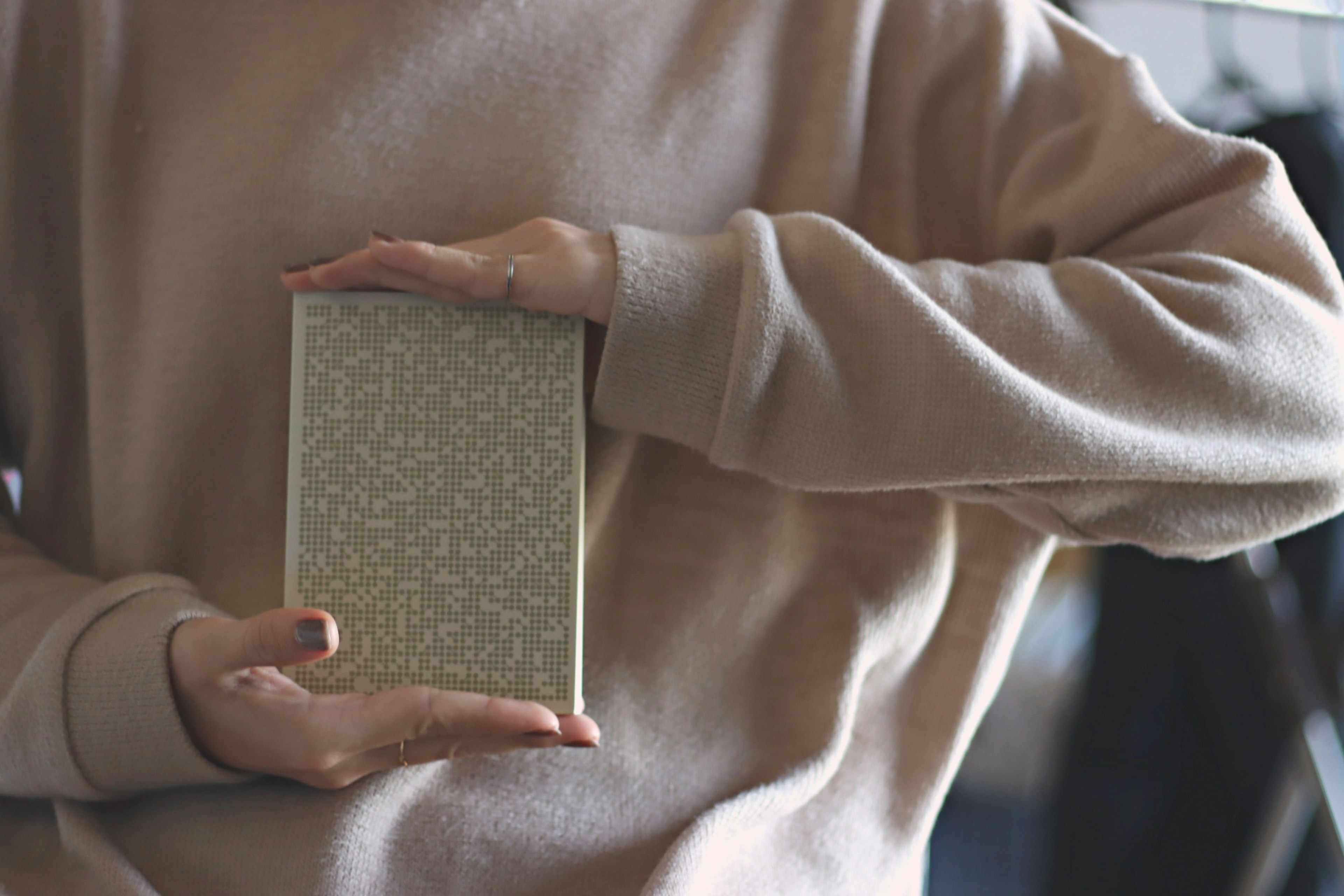 Person wearing a soft sweater holding a small gray book with both hands