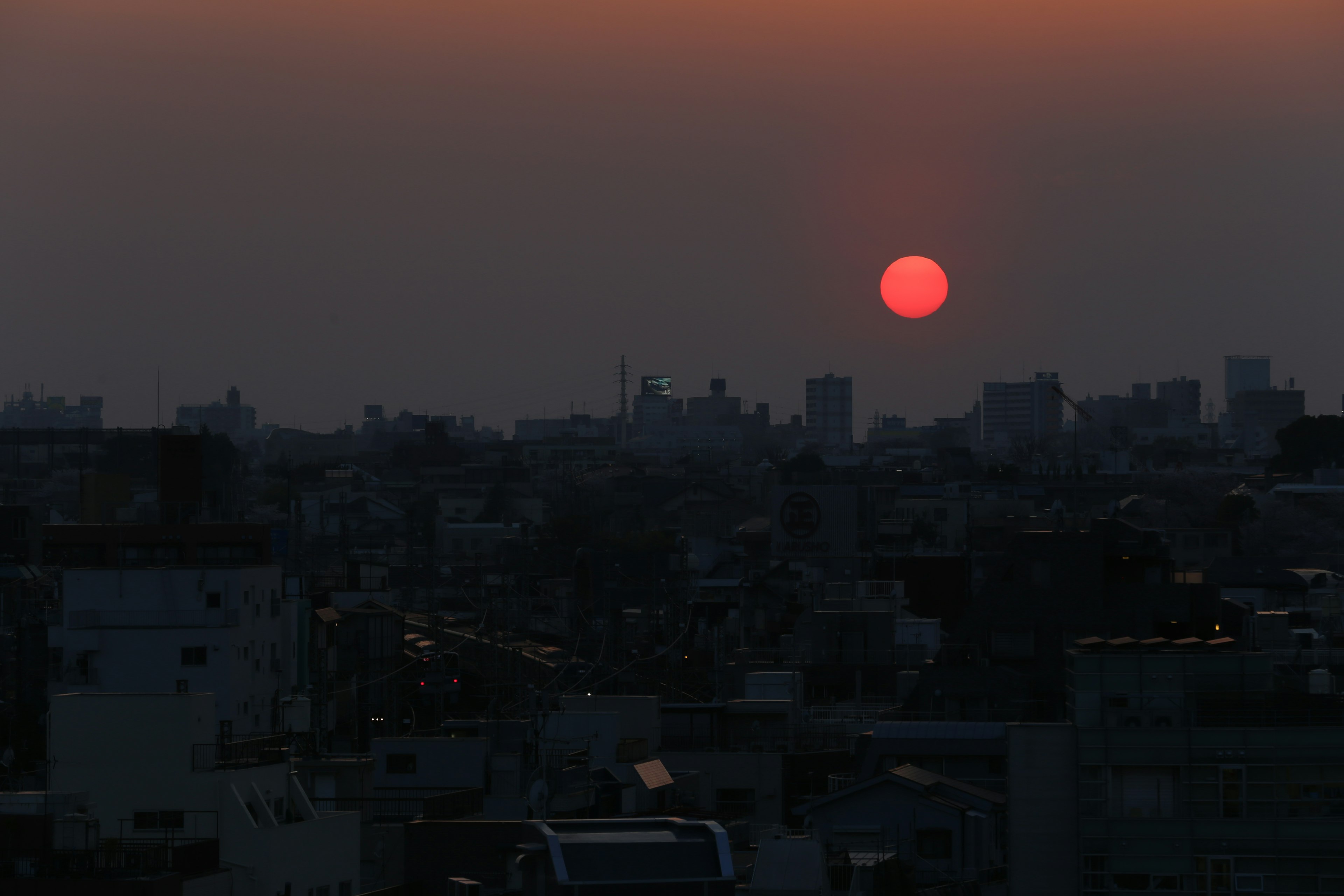 Cityscape at sunset with a large red sun on the horizon