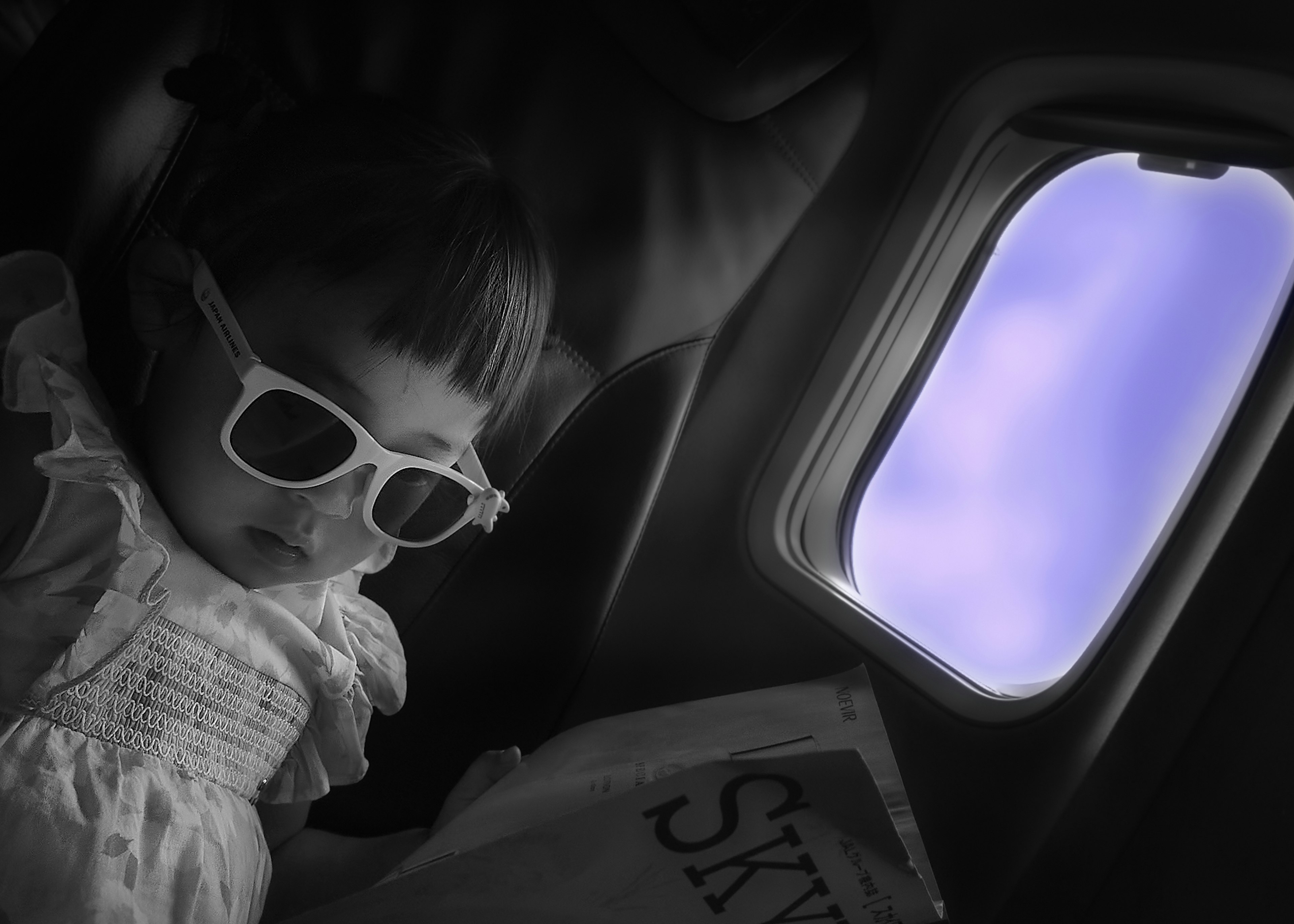 Enfant portant des lunettes de soleil lisant un livre dans un avion