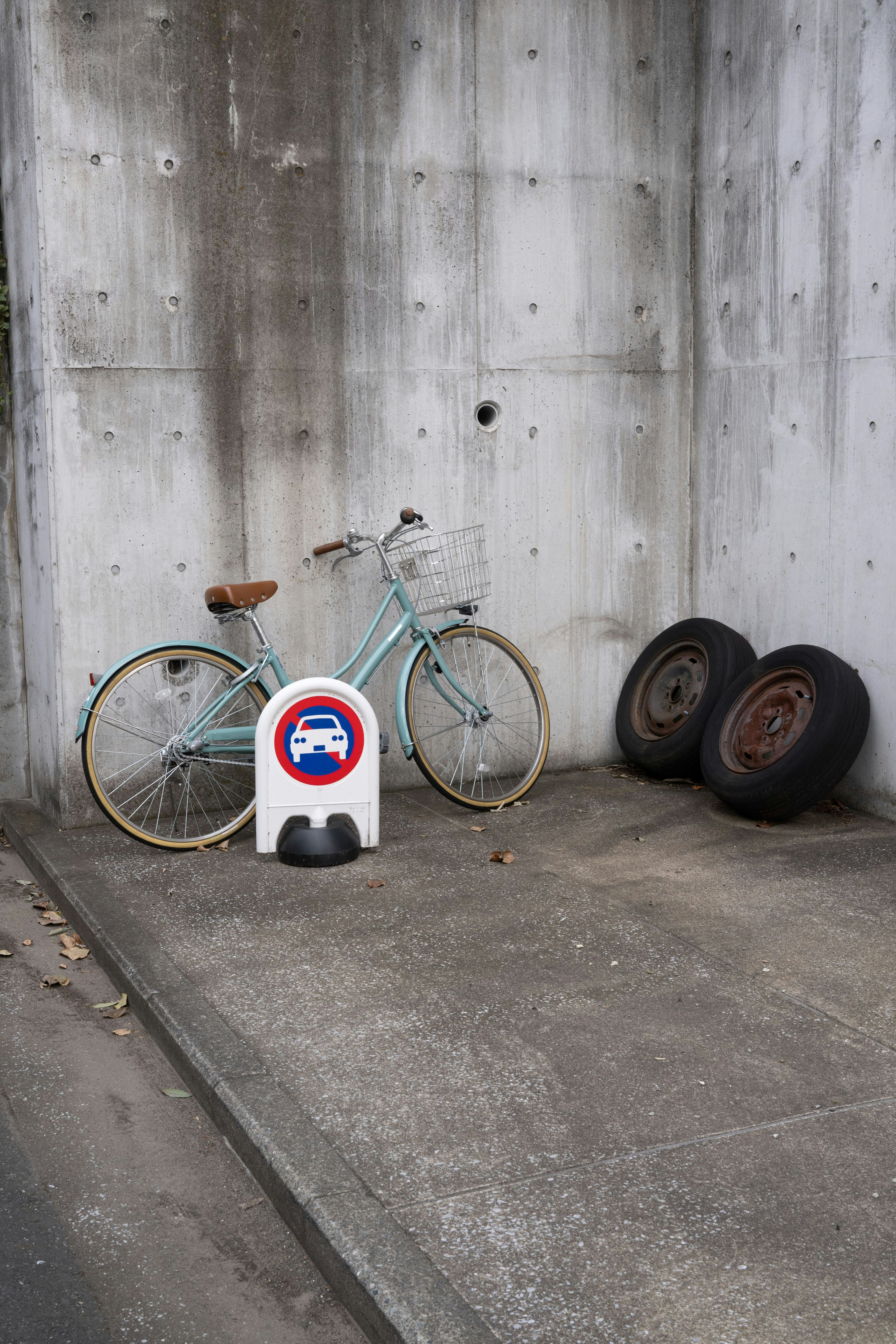 Una bicicletta blu appoggiata a un muro di cemento accanto a un insieme di vecchi pneumatici