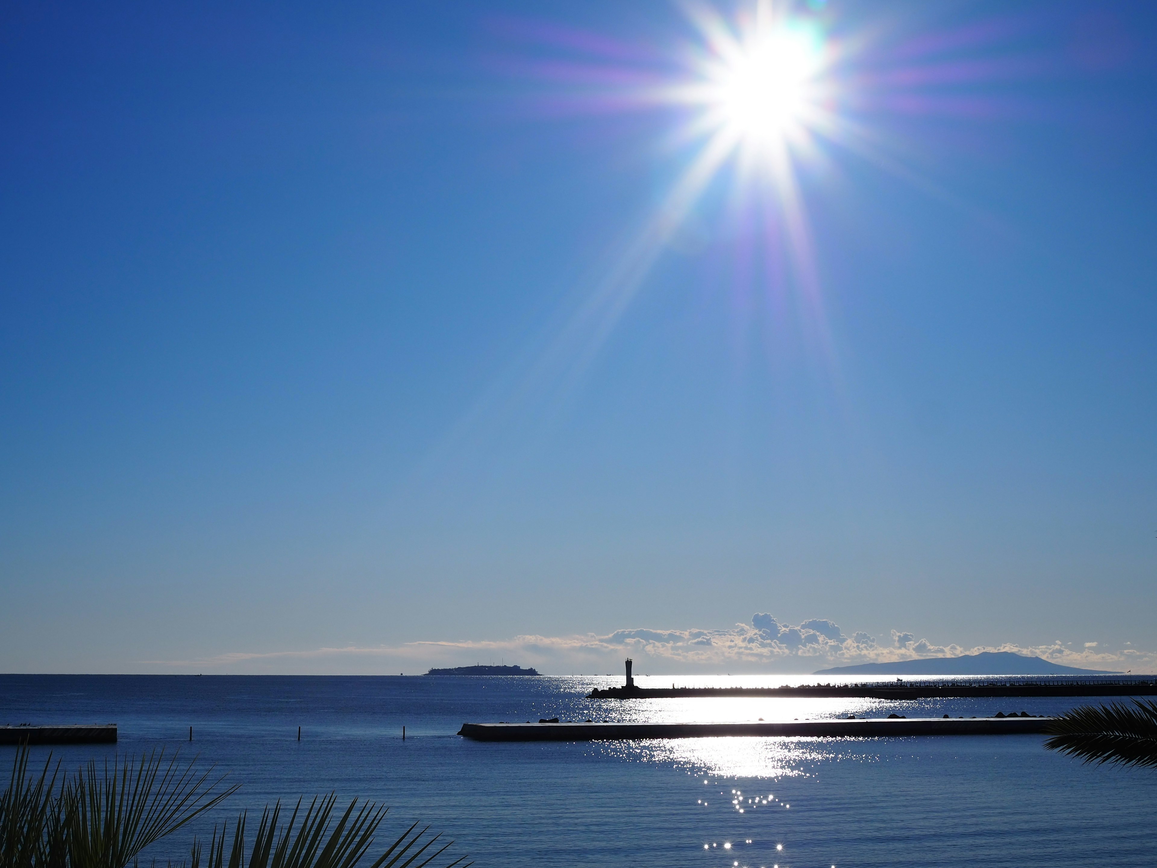 Bright sun over a calm blue sea with a lighthouse and shimmering water