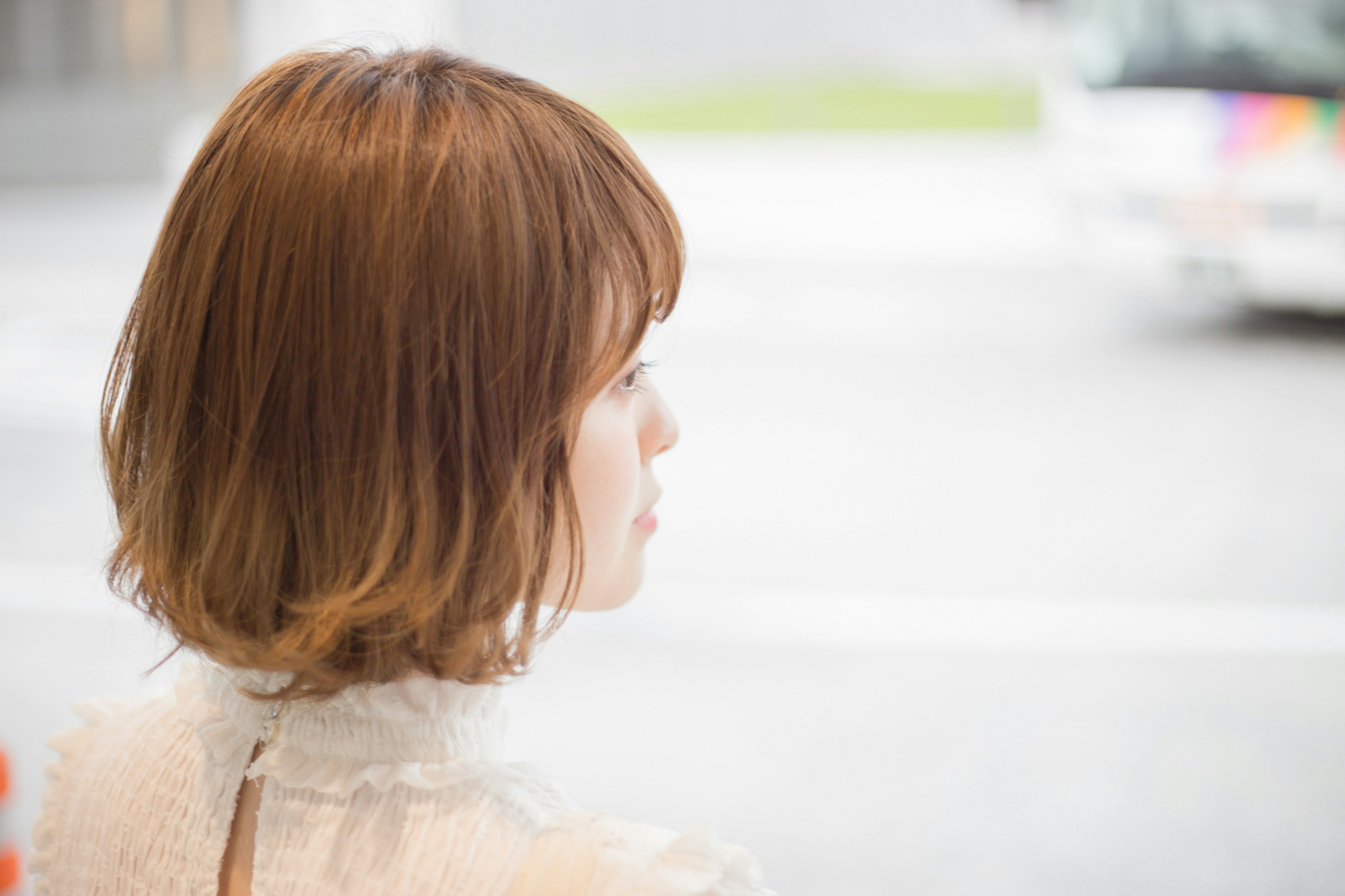 A young woman with a bob hairstyle facing away wearing a light-colored outfit