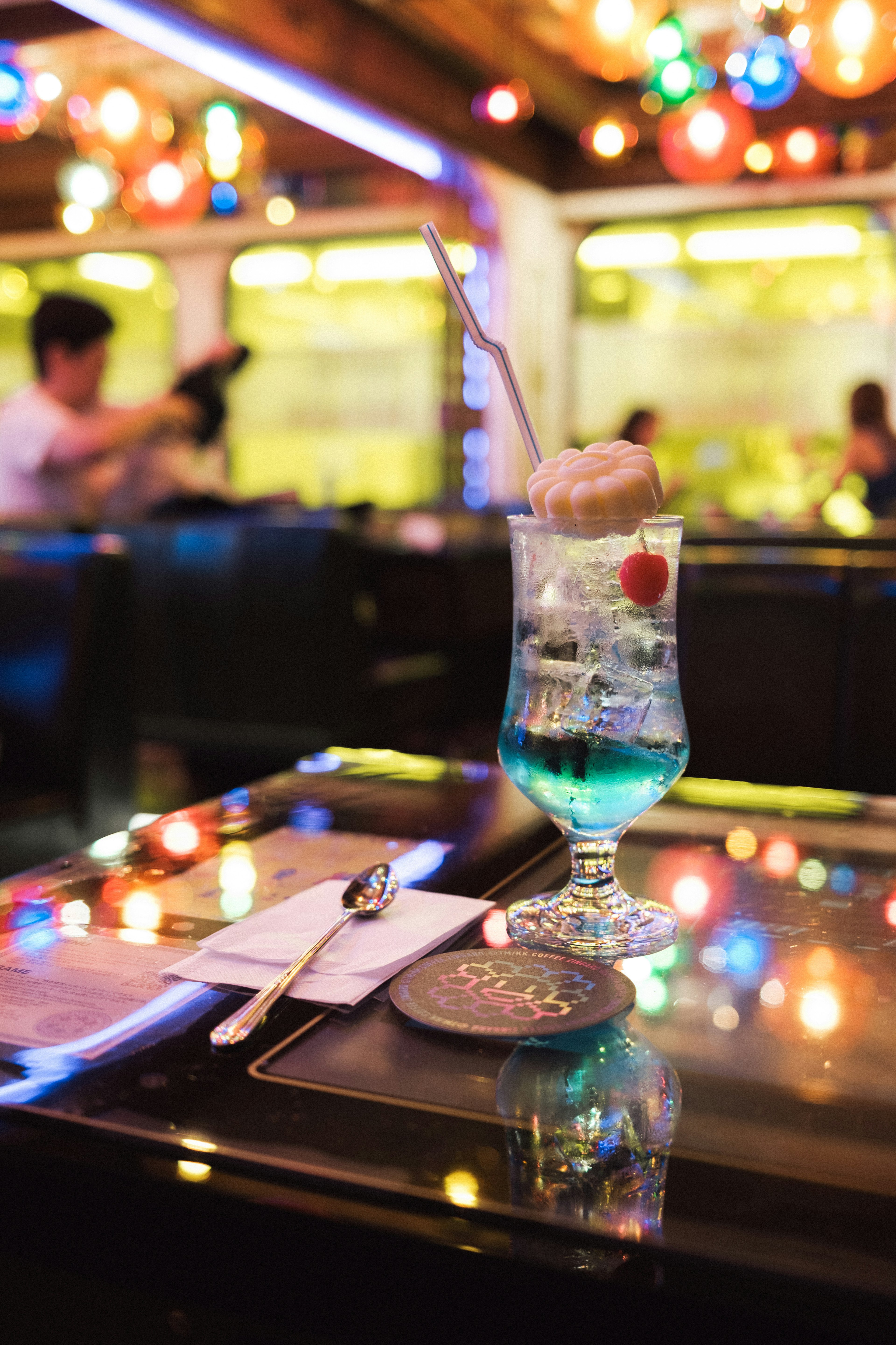 A vibrant blue cocktail with ice cream and cherry under colorful lights