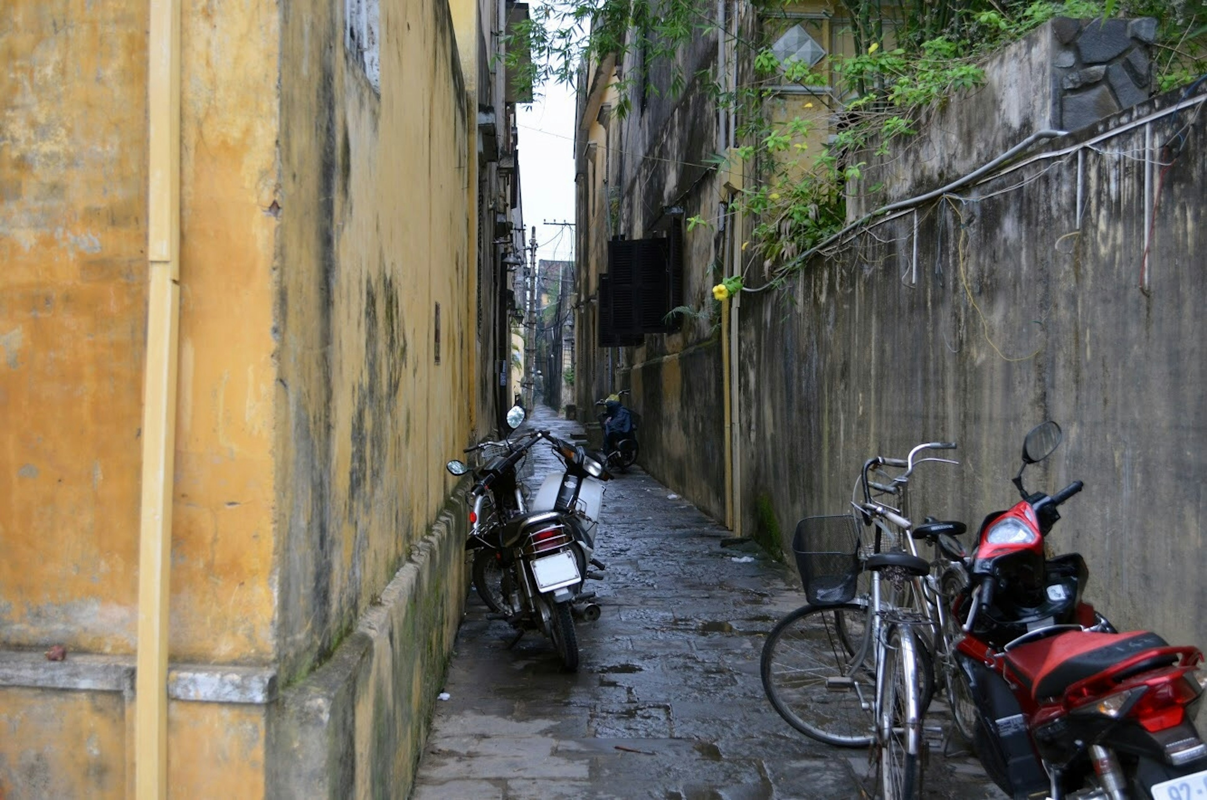 Vicolo stretto con motociclette e biciclette parcheggiate circondato da vecchi muri