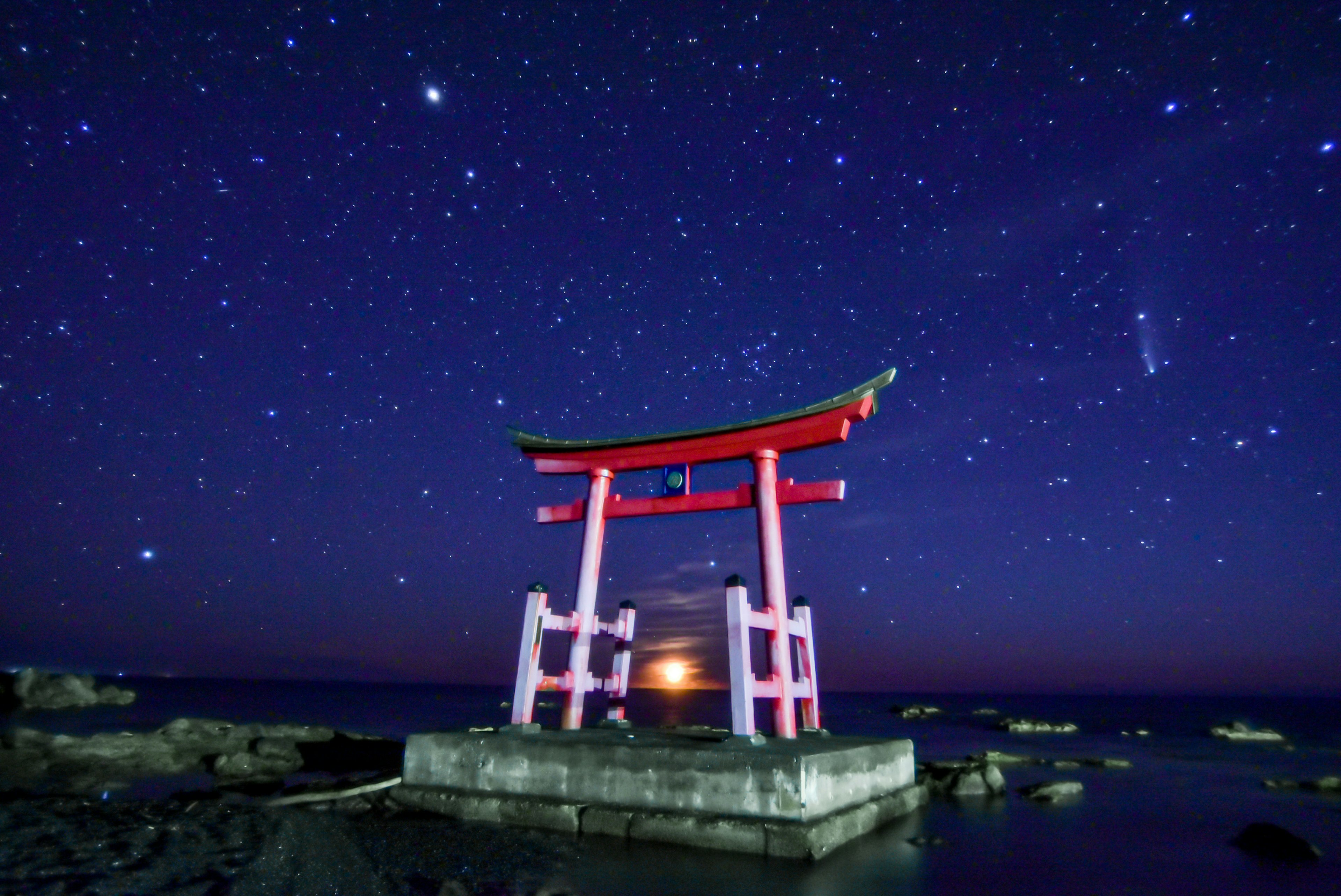 Un torii rouge se dresse contre un ciel nocturne étoilé avec un coucher de soleil