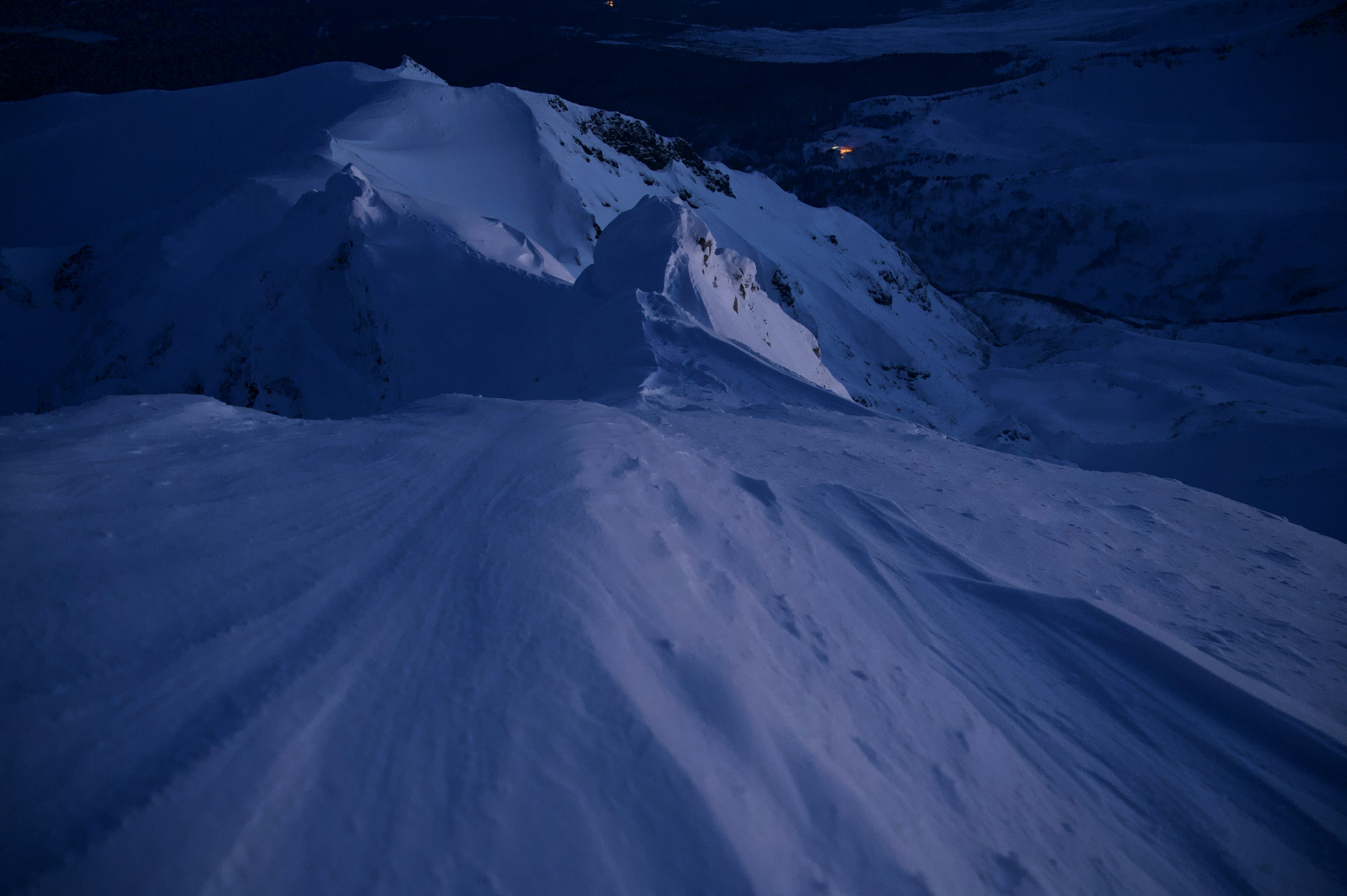 暗い夜の雪山の風景で、滑らかな雪の斜面が広がり、山の頂上が少しだけ見える