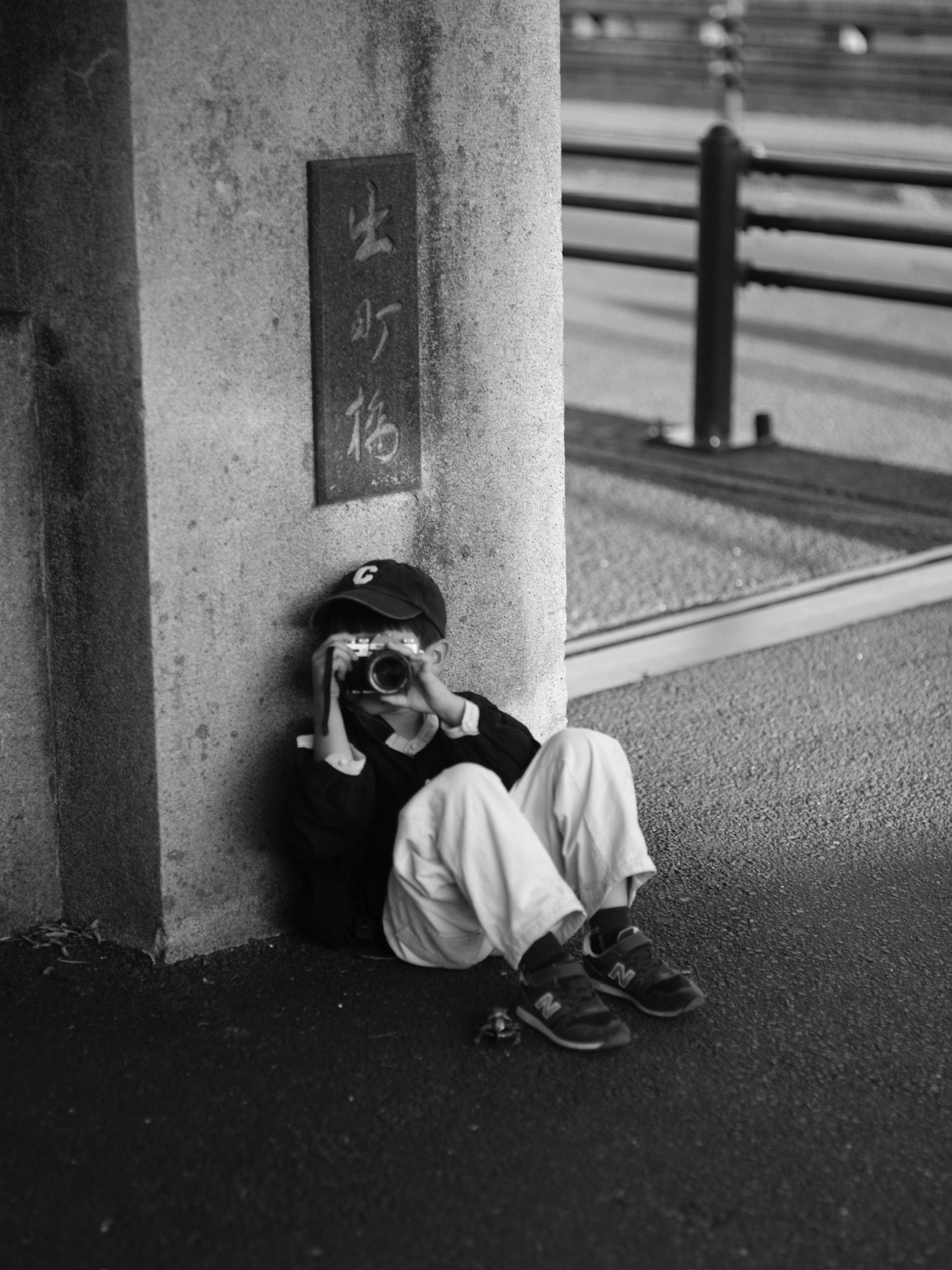 Foto in bianco e nero di un bambino seduto vicino a un pilastro con una macchina fotografica