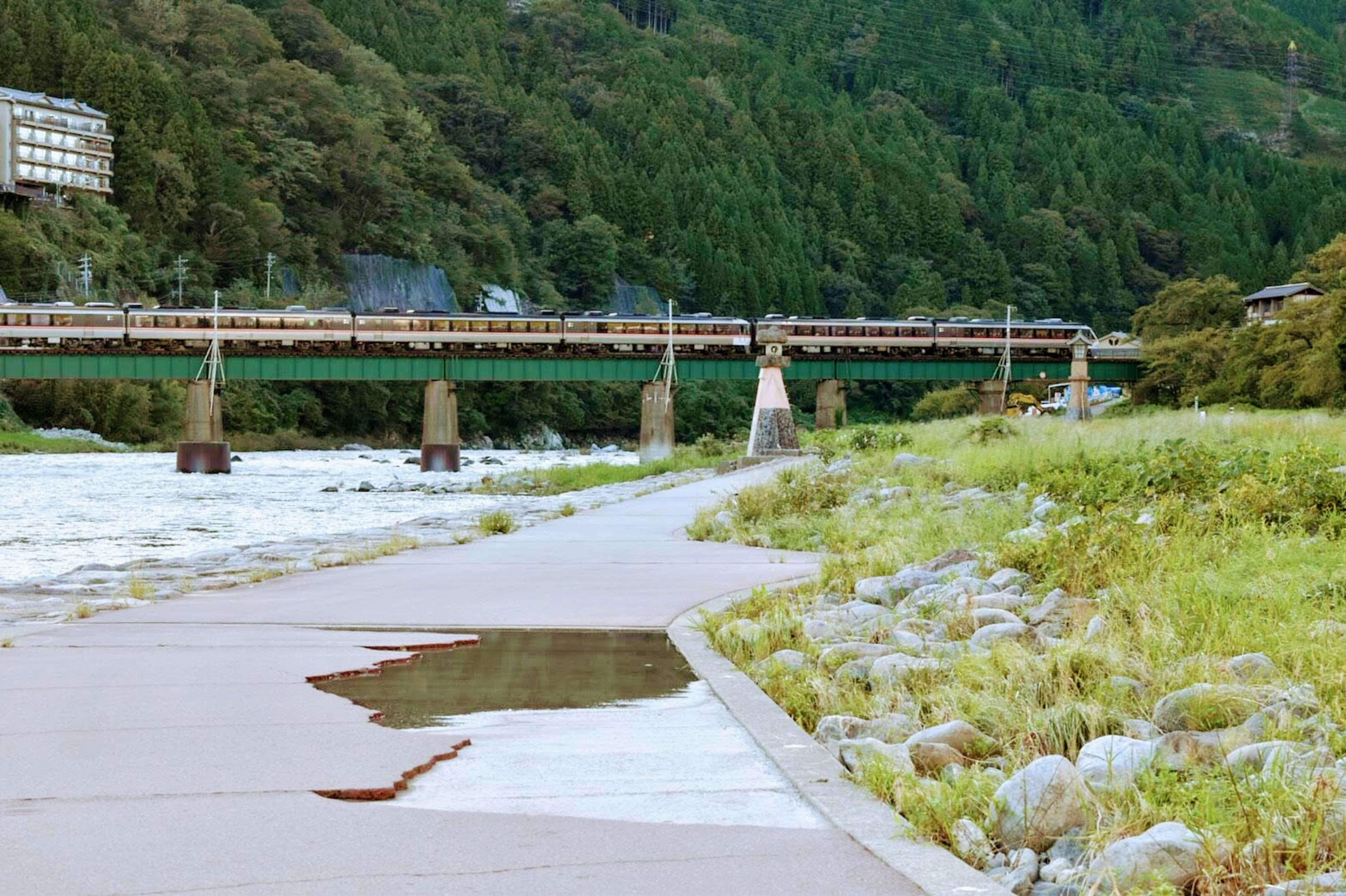 Riverside walkway and railway bridge surrounded by green mountains