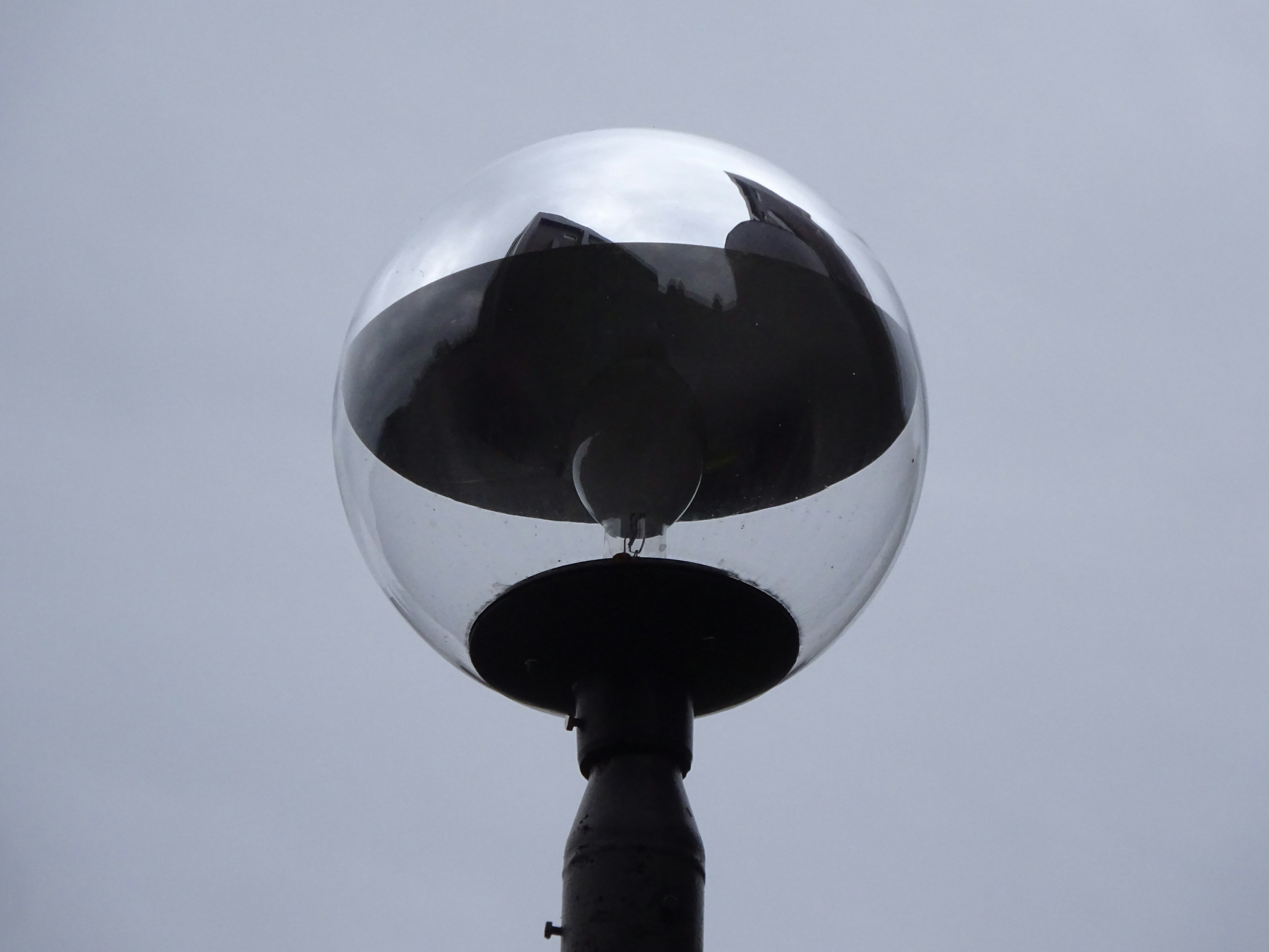 A metallic spherical object mounted on a pole against a gray sky