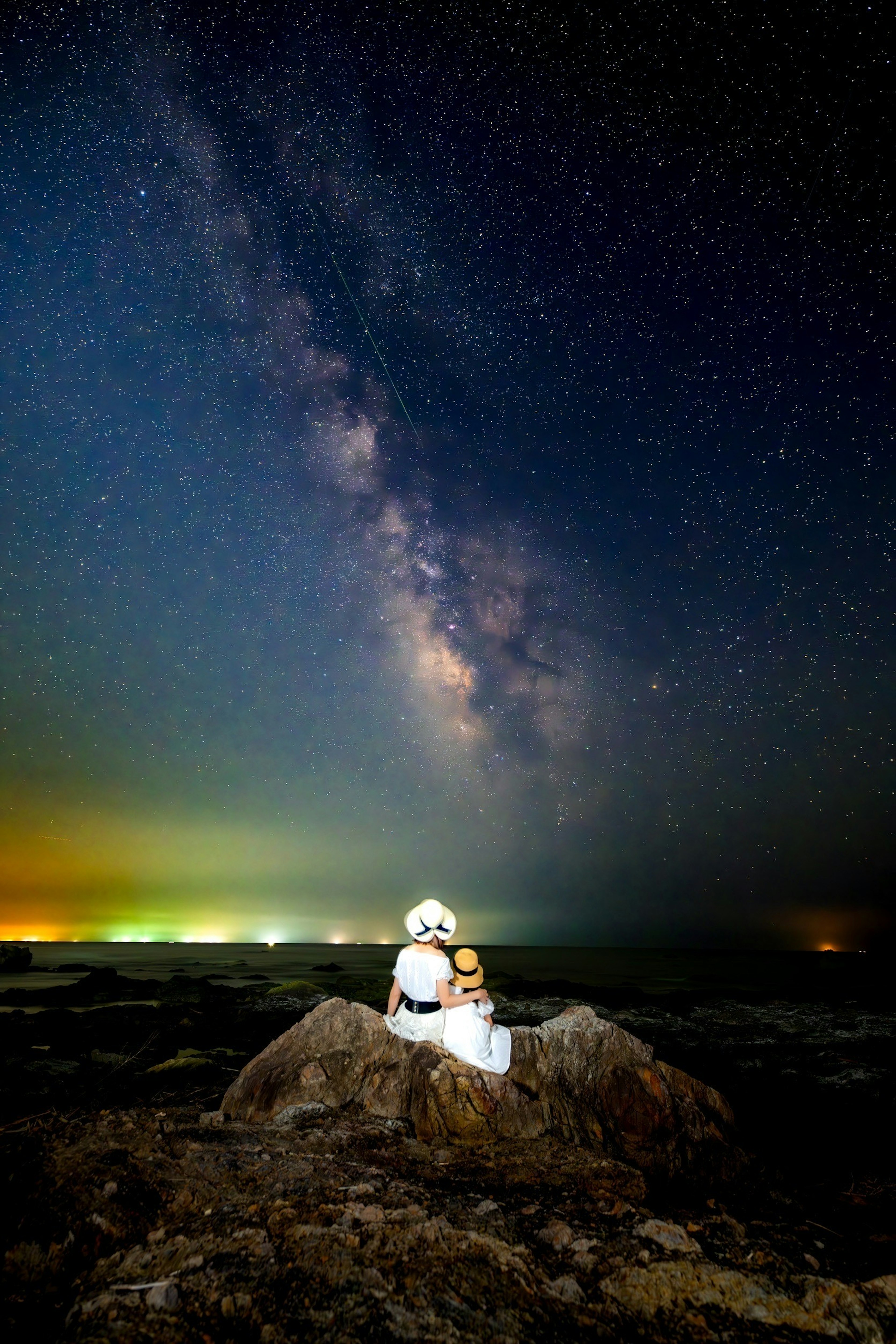 星空の下で座る二人の人物と岩の風景