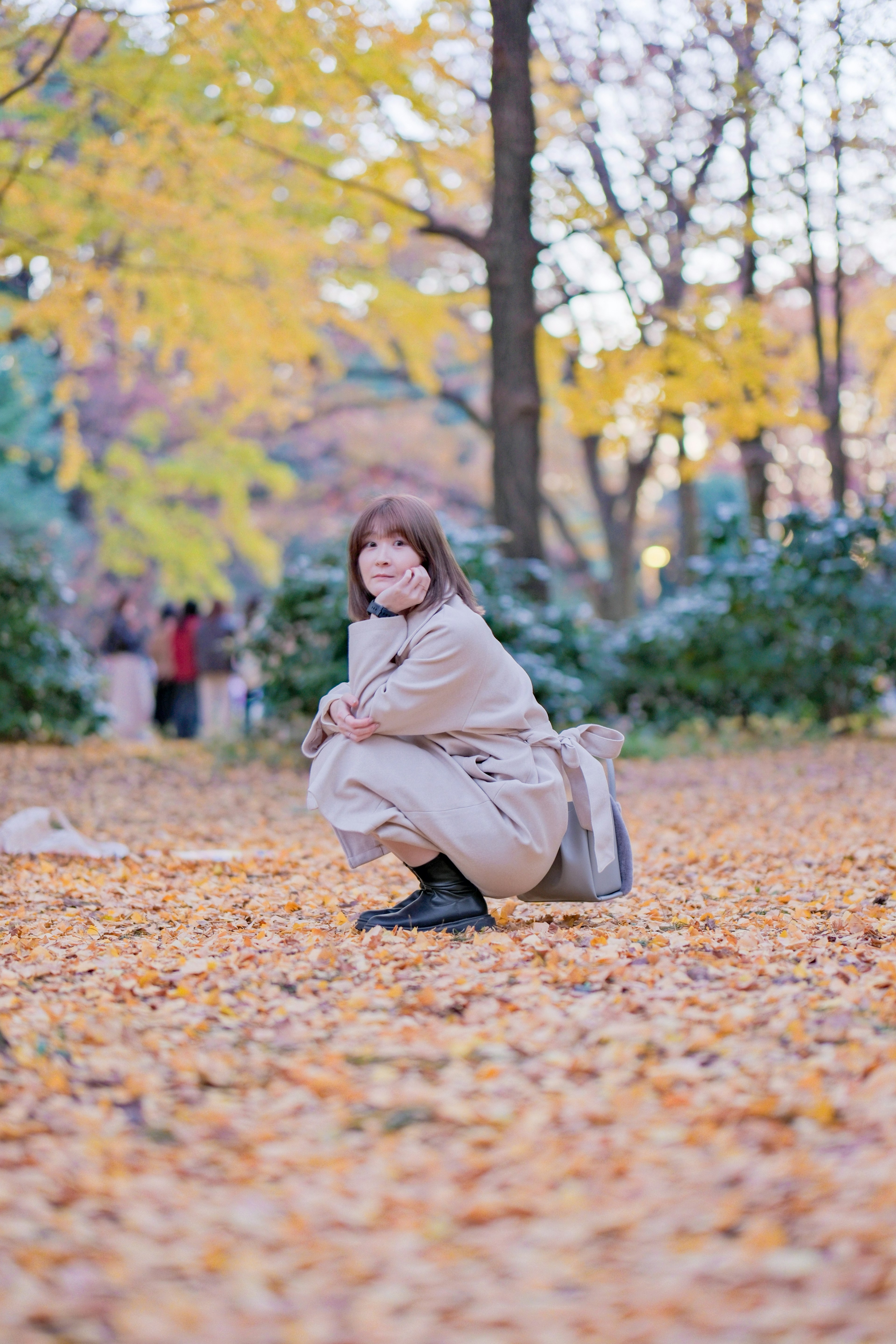 秋の公園で笑顔の女性が落ち葉の上にしゃがんでいる