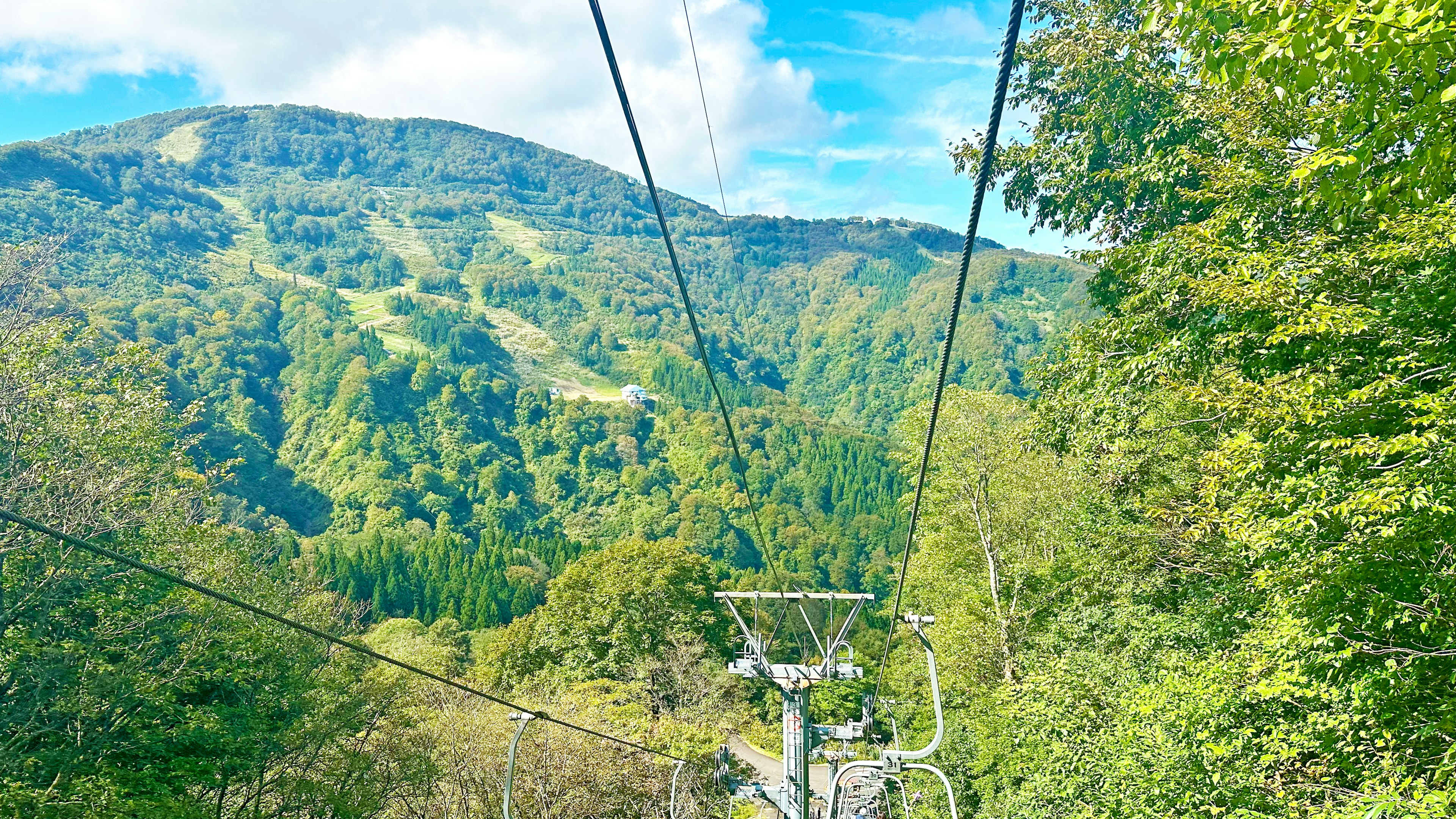 Pemandangan indah dari kereta gantung yang menghadap pegunungan hijau dan langit biru