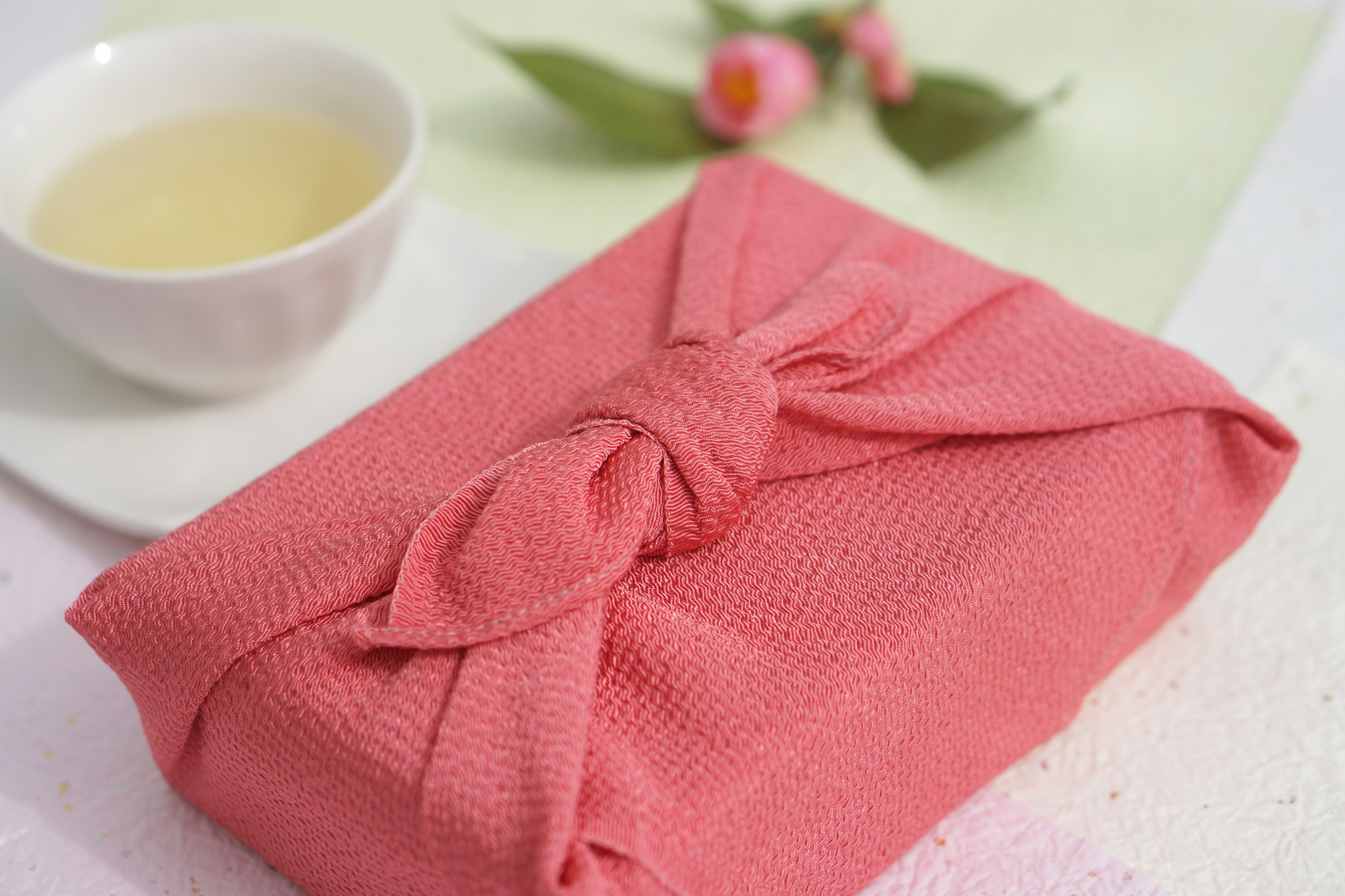 A pink fabric-wrapped gift next to a white tea bowl