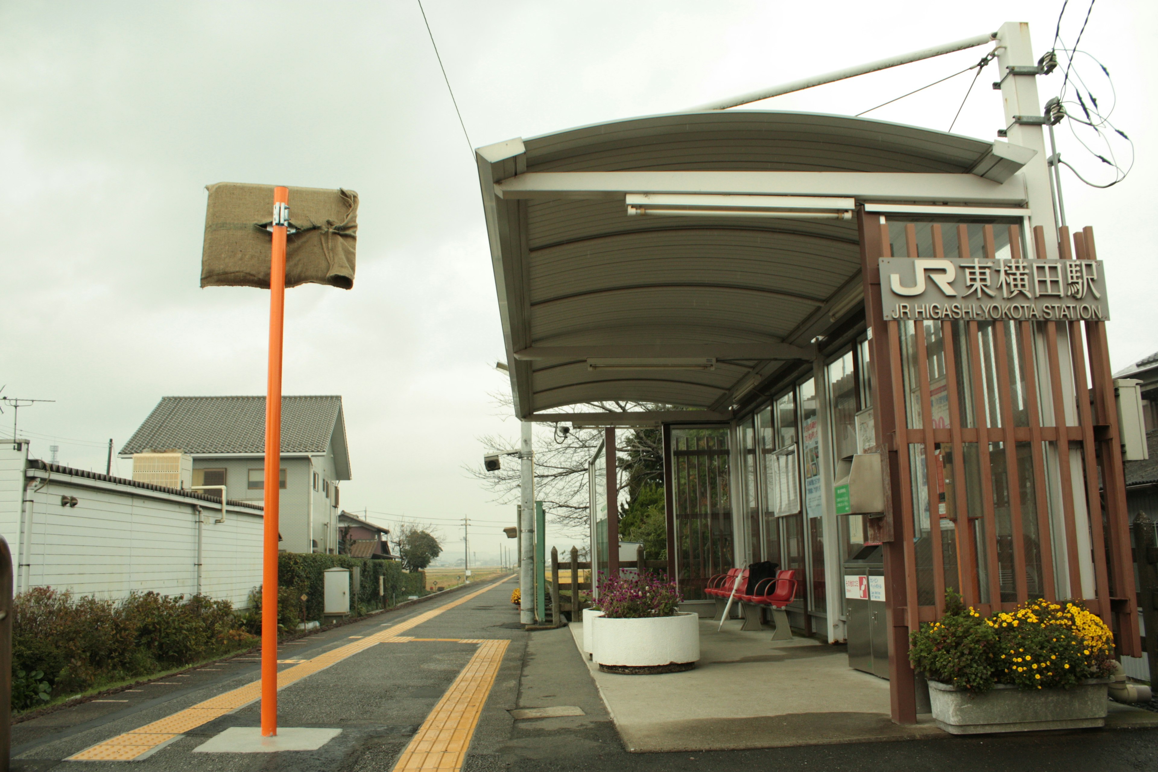 駅の外観と屋根のあるプラットフォーム 橙色の標識と周囲の住宅が見える