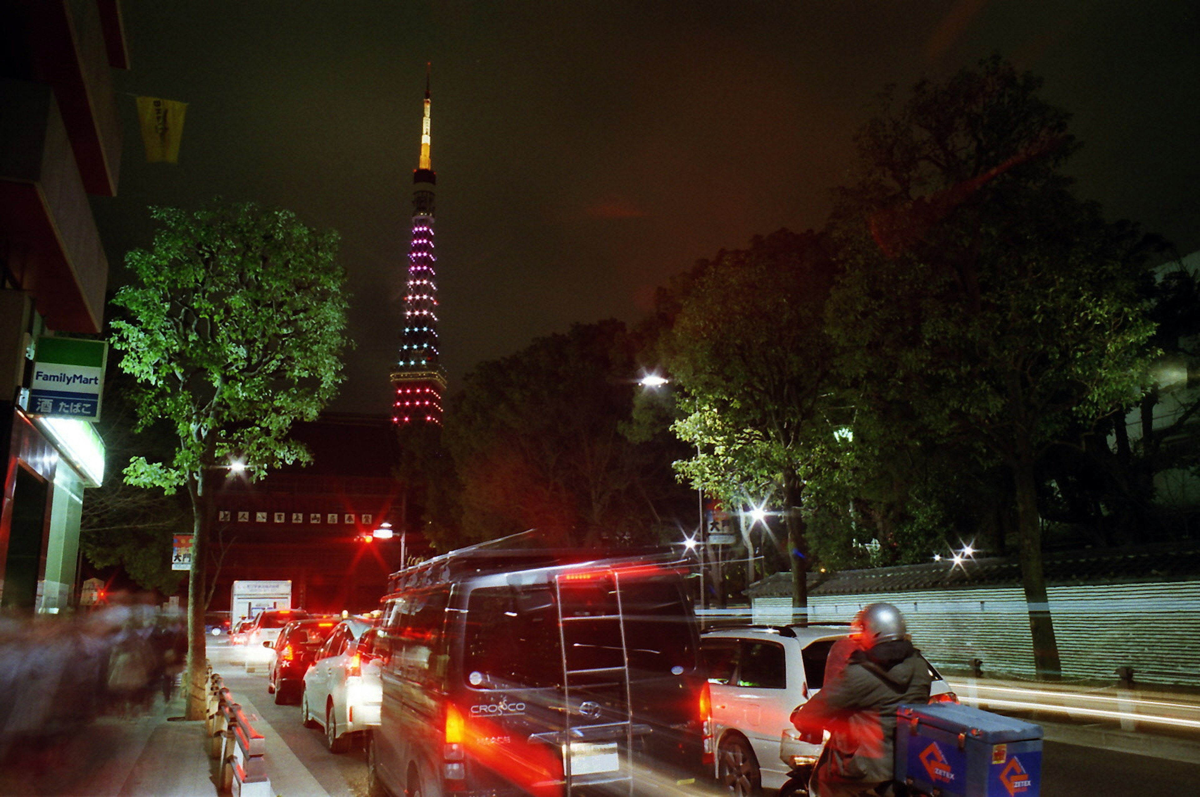 Night view of Tokyo Tower illuminated in colorful lights with traffic in the foreground