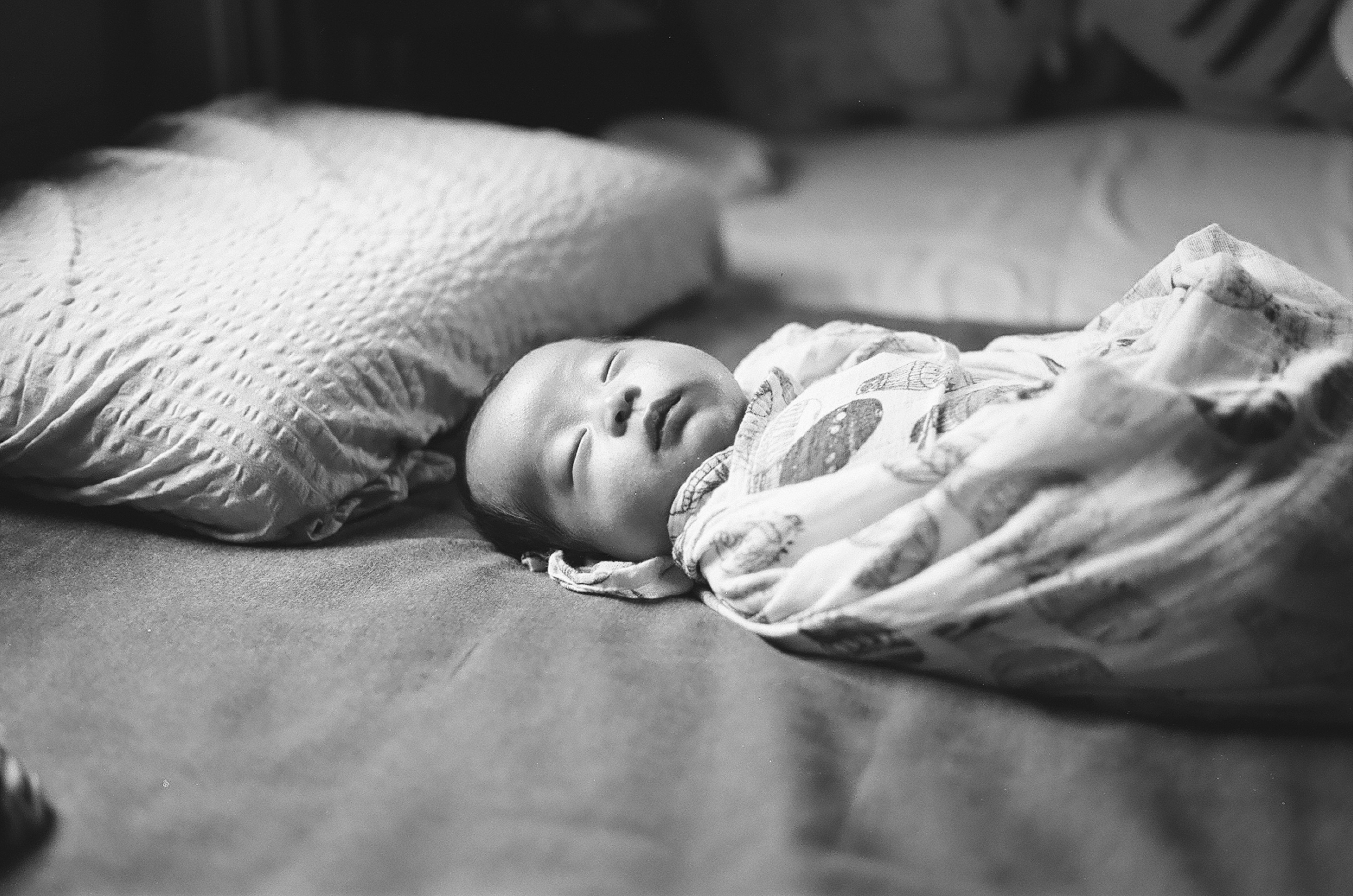 A baby sleeping on a bed with a pillow in black and white