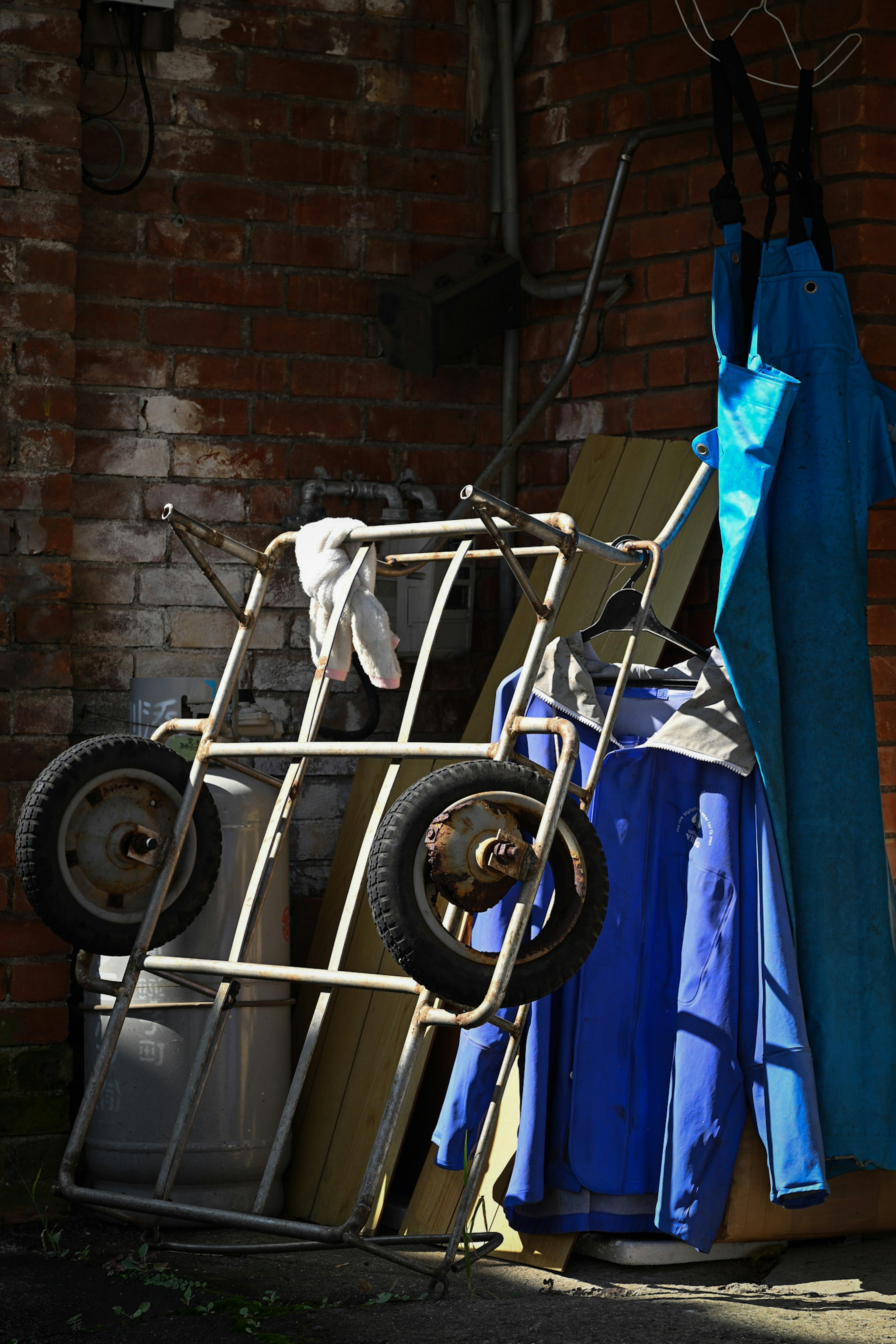 A cart leaning against a wall with blue work clothes hanging nearby