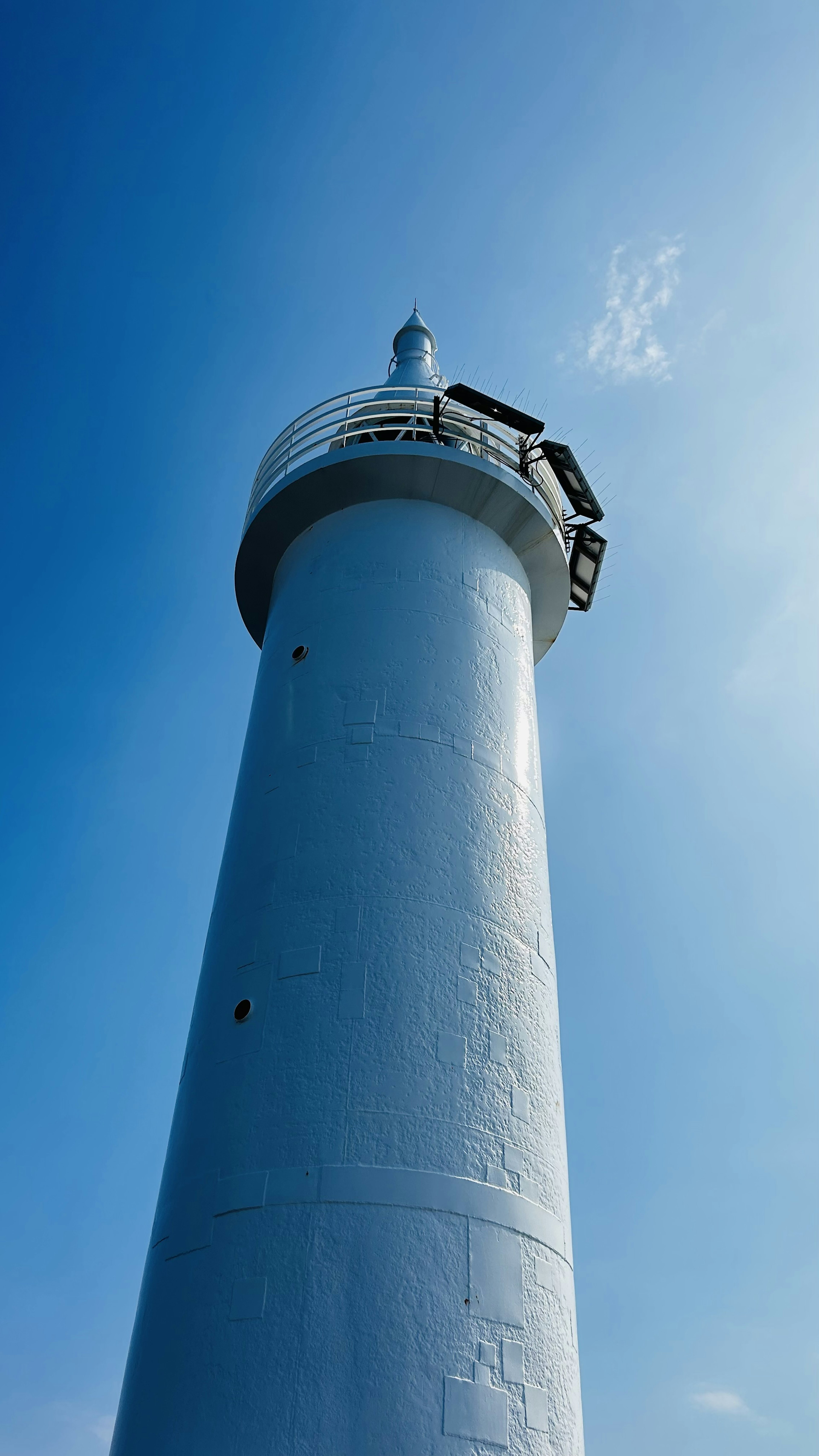 A white lighthouse under a blue sky with a clear view of its top