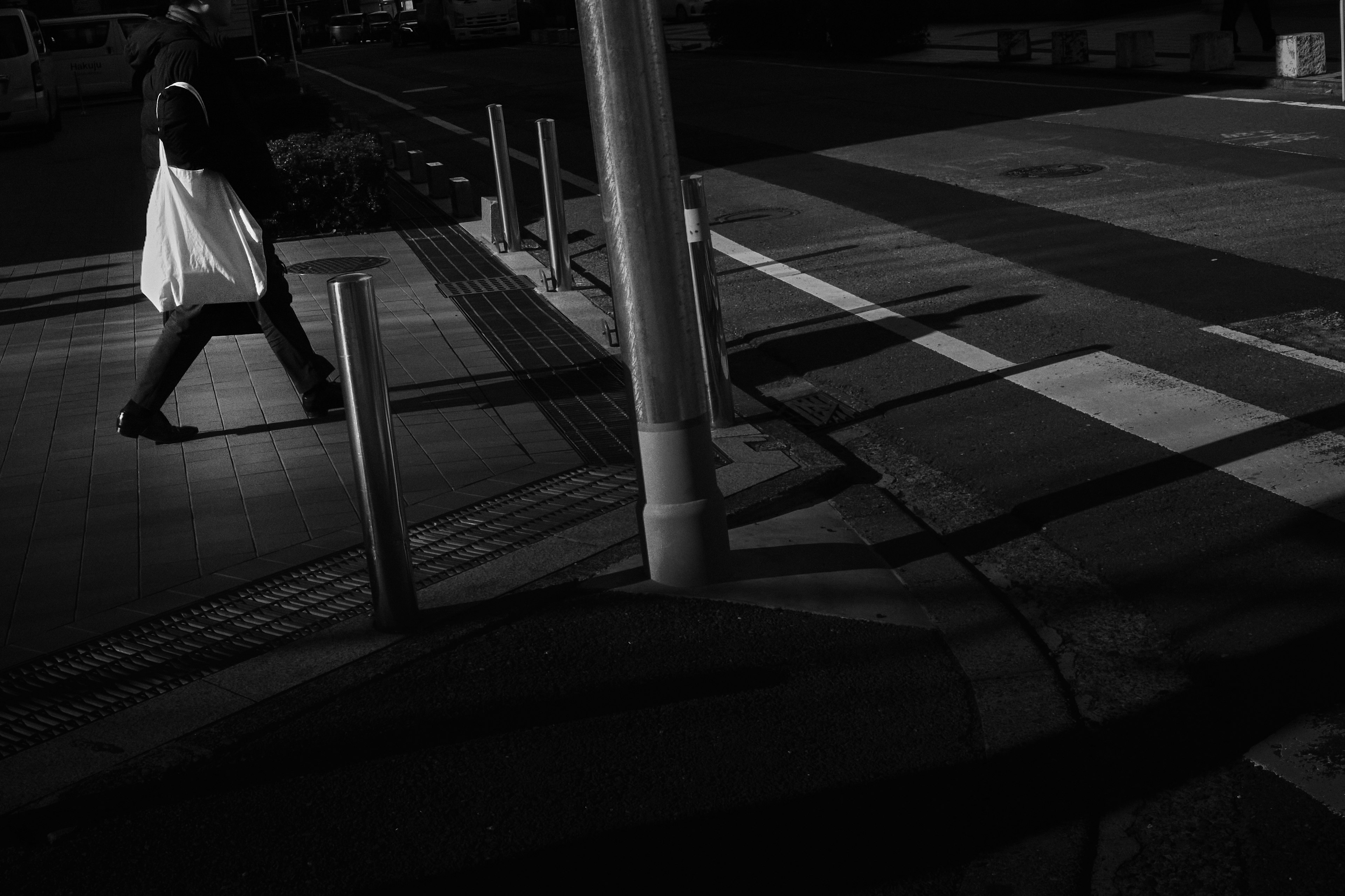 A person carrying a white bag walking across a crosswalk with shadows