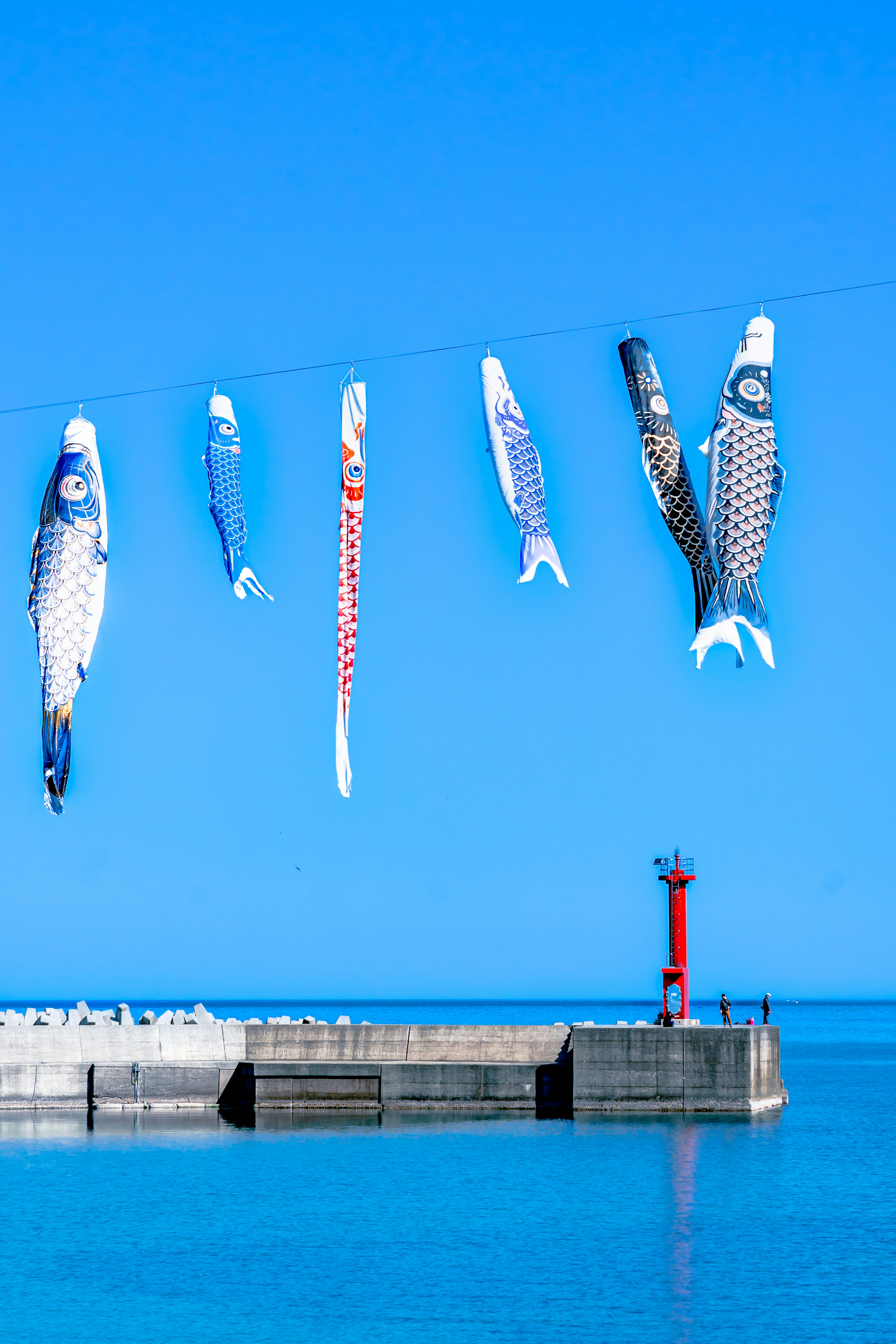 青空の下で吊るされた色とりどりの魚の飾りと赤い灯台がある港