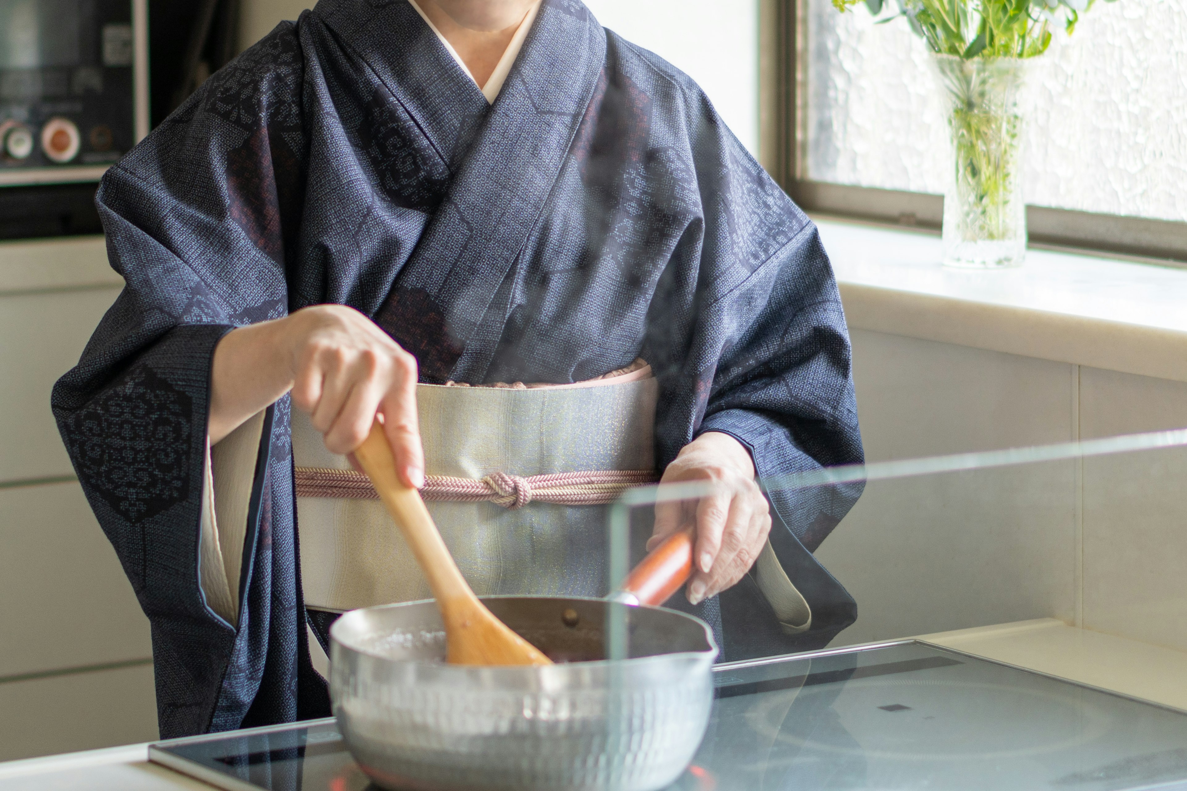 A woman in a kimono stirring a pot in a modern kitchen