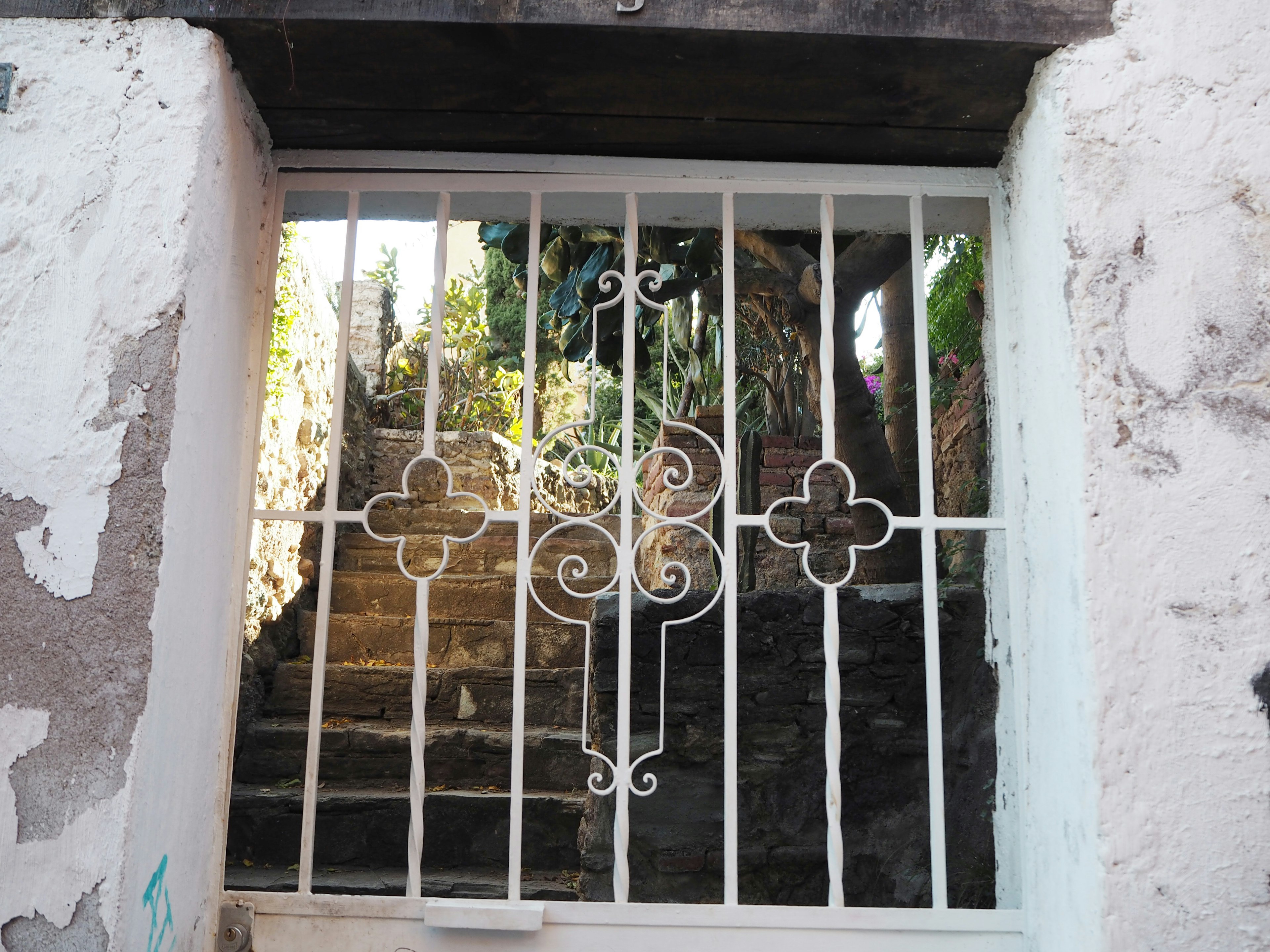 Puerta de hierro blanco que revela escaleras detrás de una pared vieja