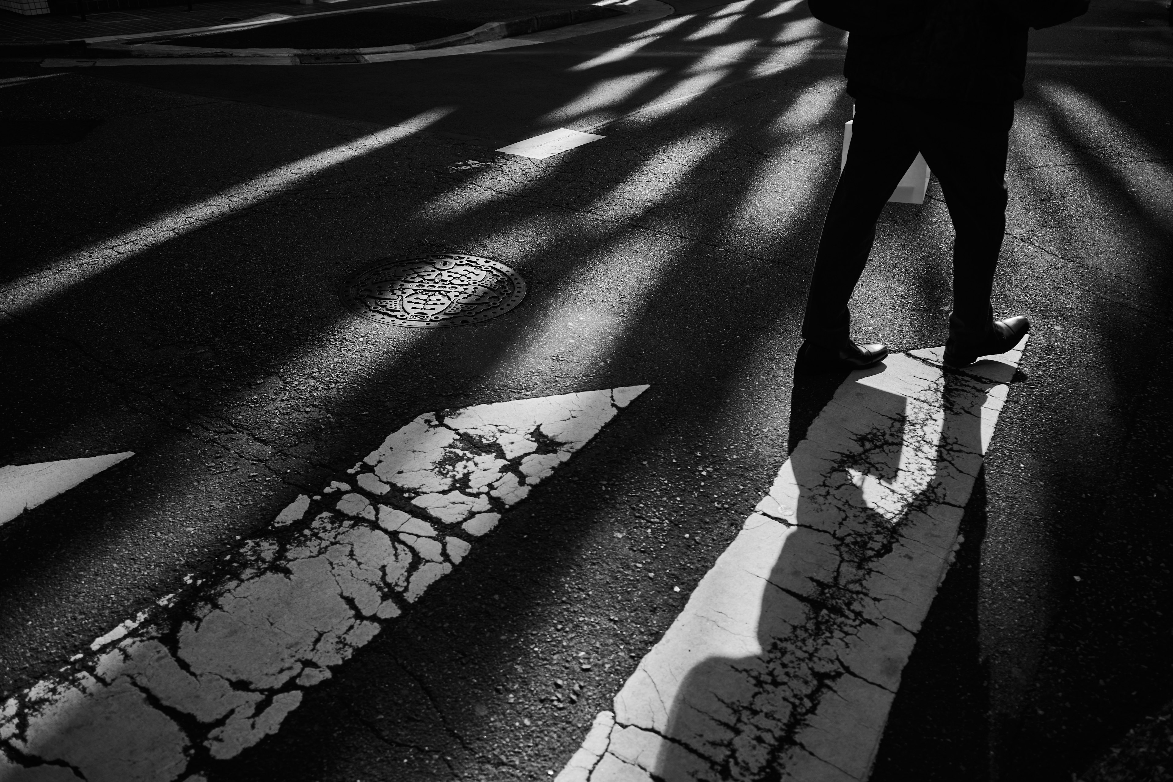 A pedestrian's feet on a crosswalk with shadows and light patterns